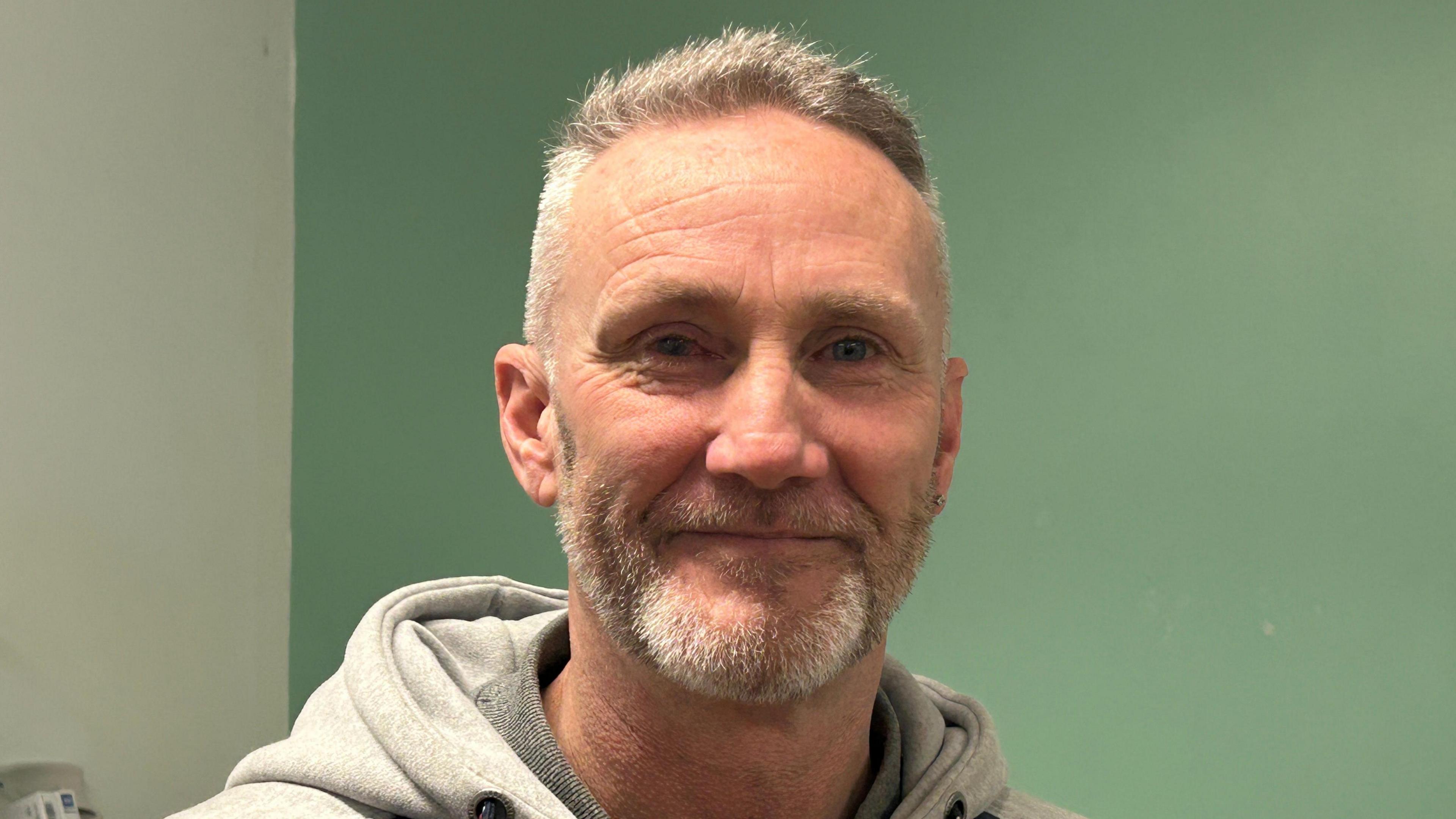 A man in a grey sweatshirt smiles at the camera