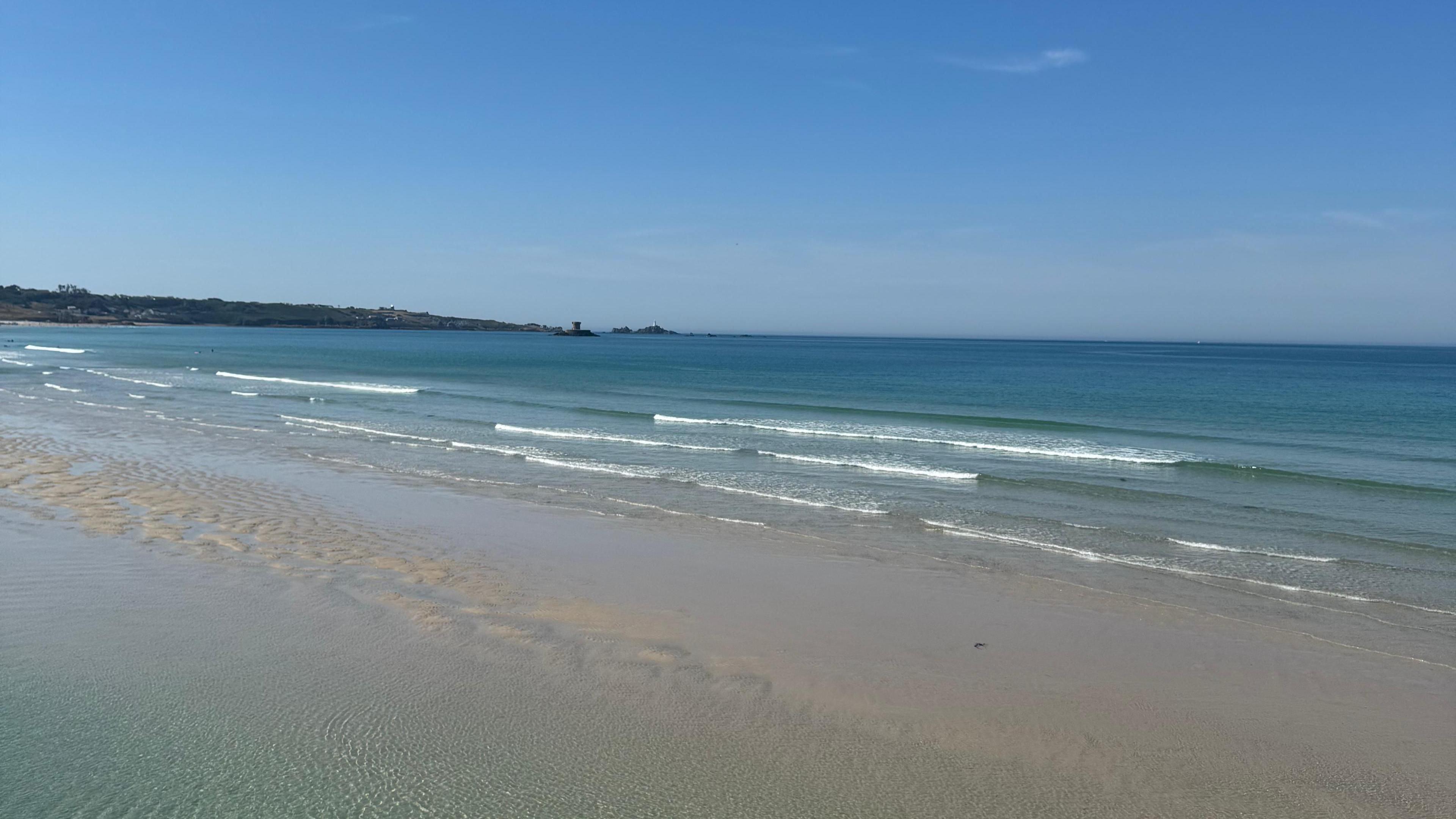 The ocean with blue skies in view, land can be seen to the left with Rocco tower in the ocean also.
