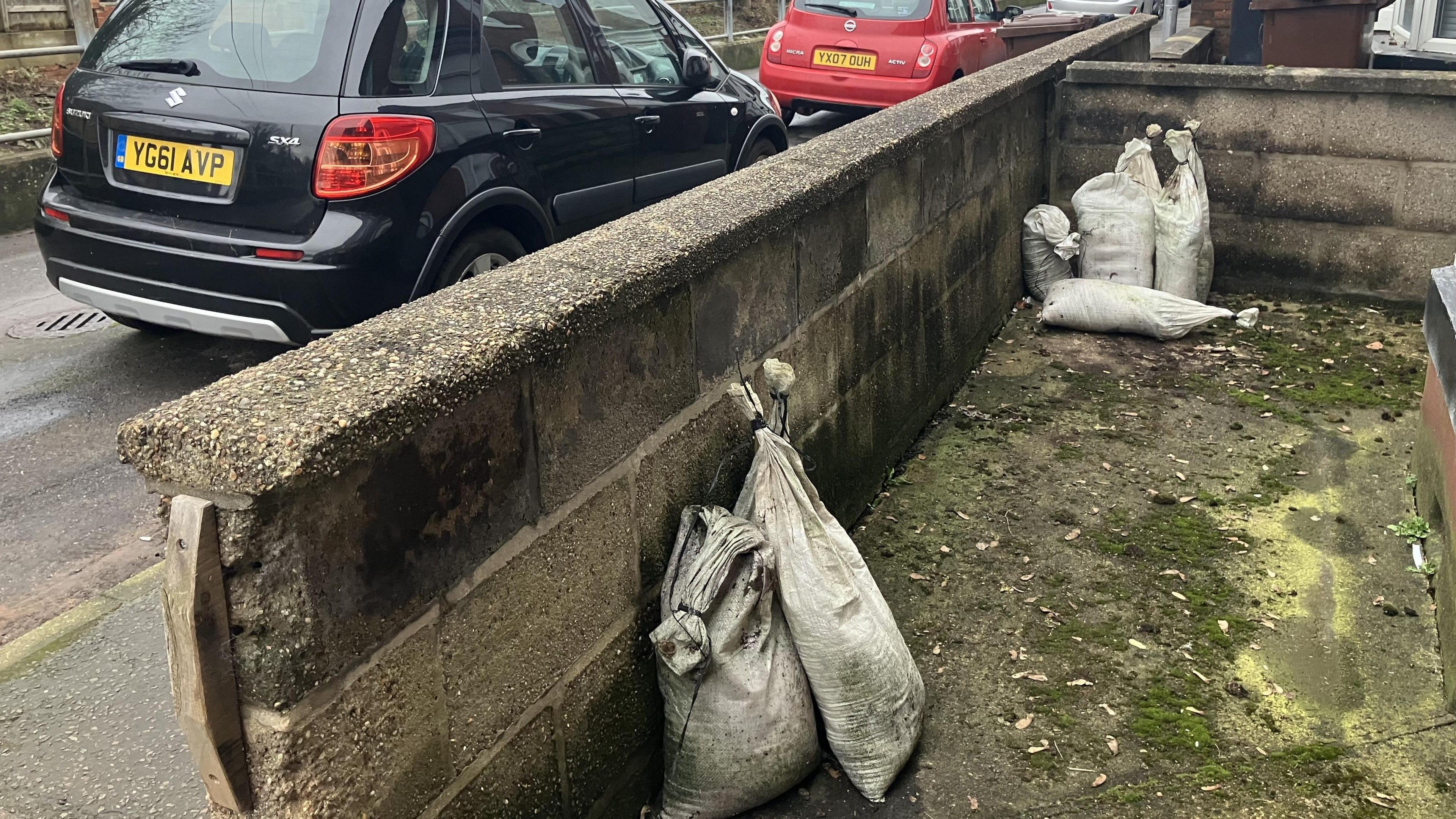 Two sandbags in the foreground behind a front wall, and another four a bit further away. Two cars are parked in the street