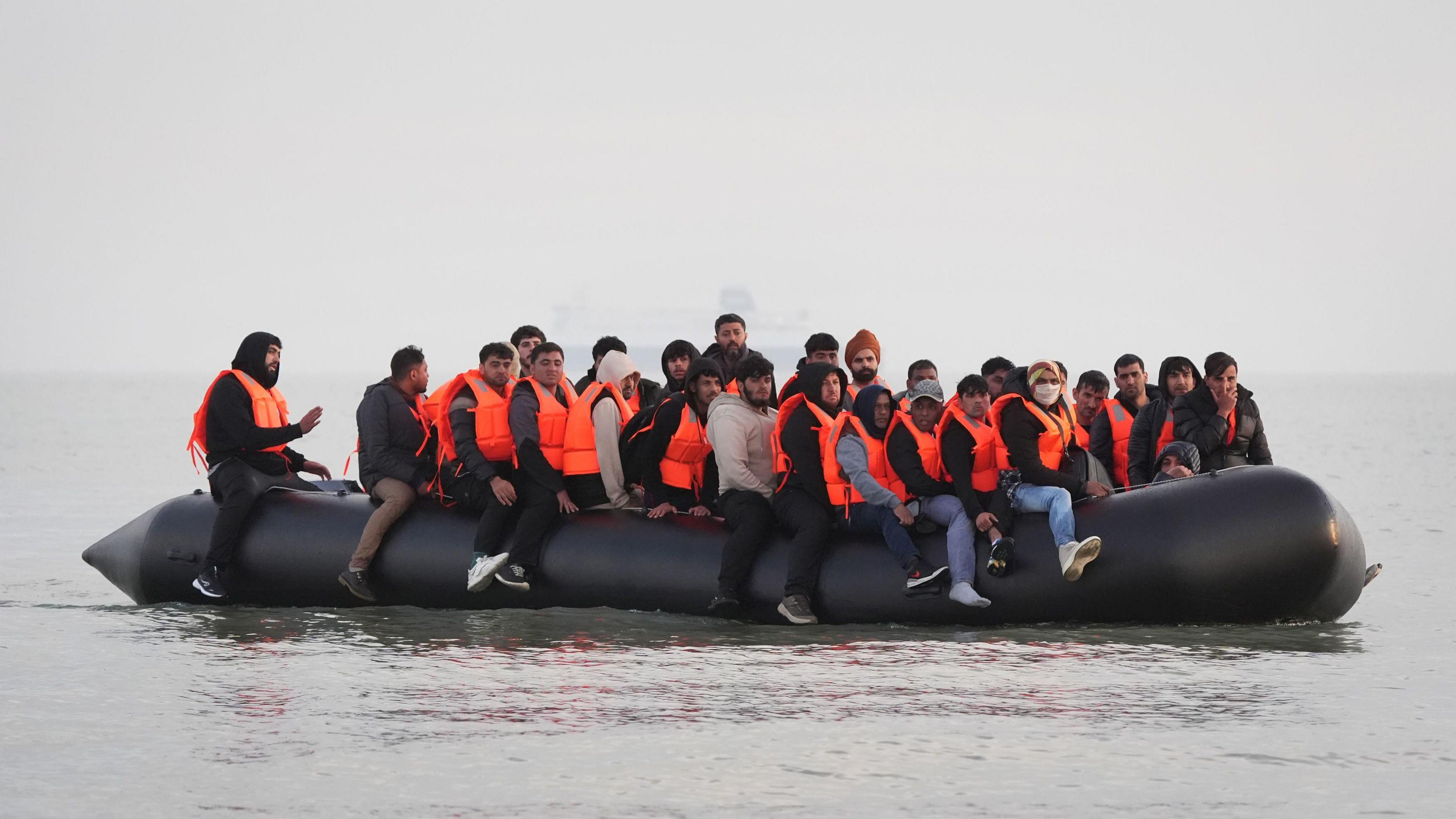 A black dinghy full of people wearing orange life jackets in the sea near Gravelines, France, on Saturday.