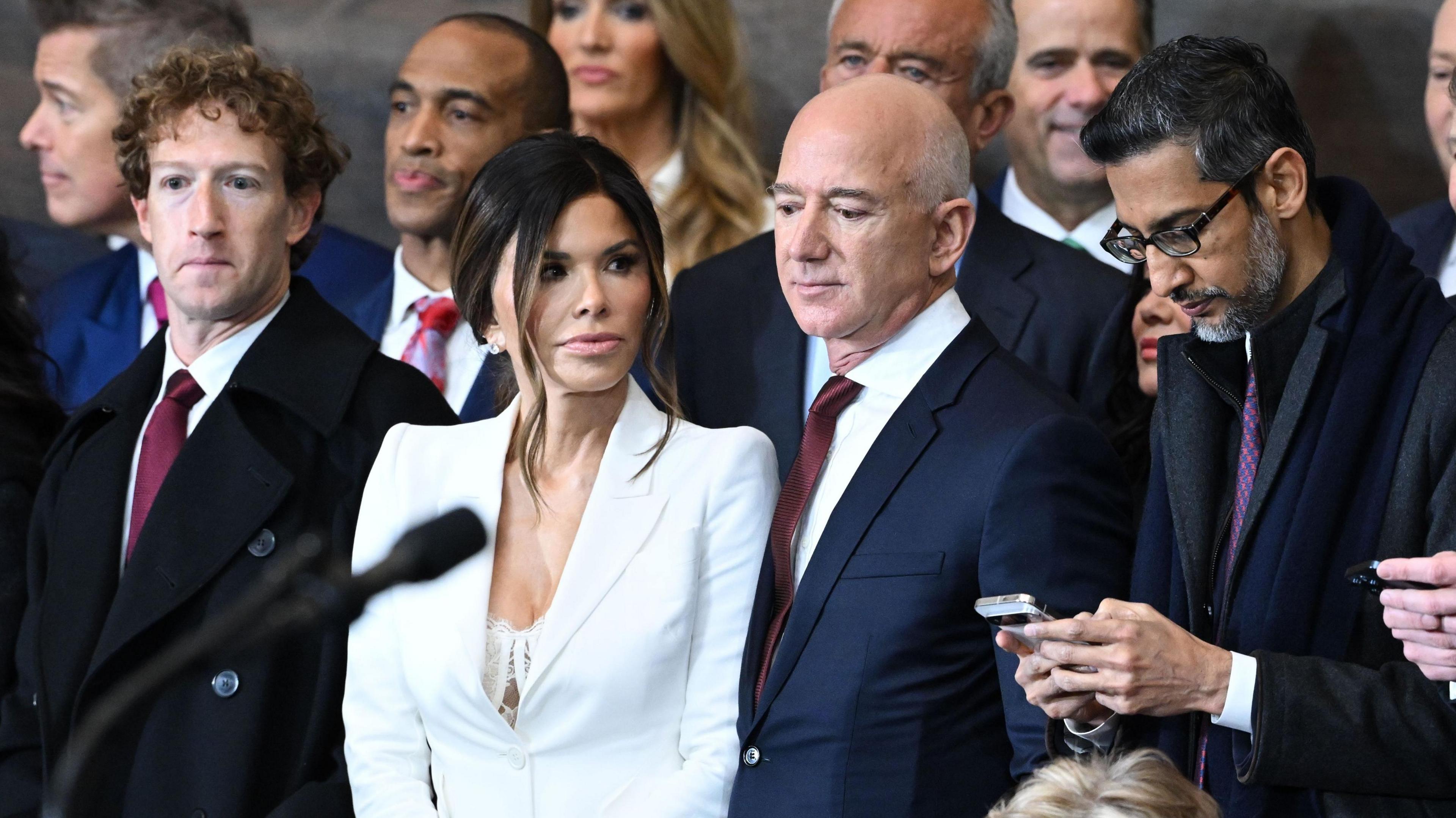 From left to right: Meta CEO Mark Zuckerberg wearing a navy suit, red neck tie and white dress shirt; Lauren Sanchez, wife of Amazon founder and former CEO Jeff Bezos, wearing a white blazer; Jeff Bezos, in a navy suit, red neck tie and white dress shirt; Google CEO Sundar Pichai, in an all black coat, shirt and tie.