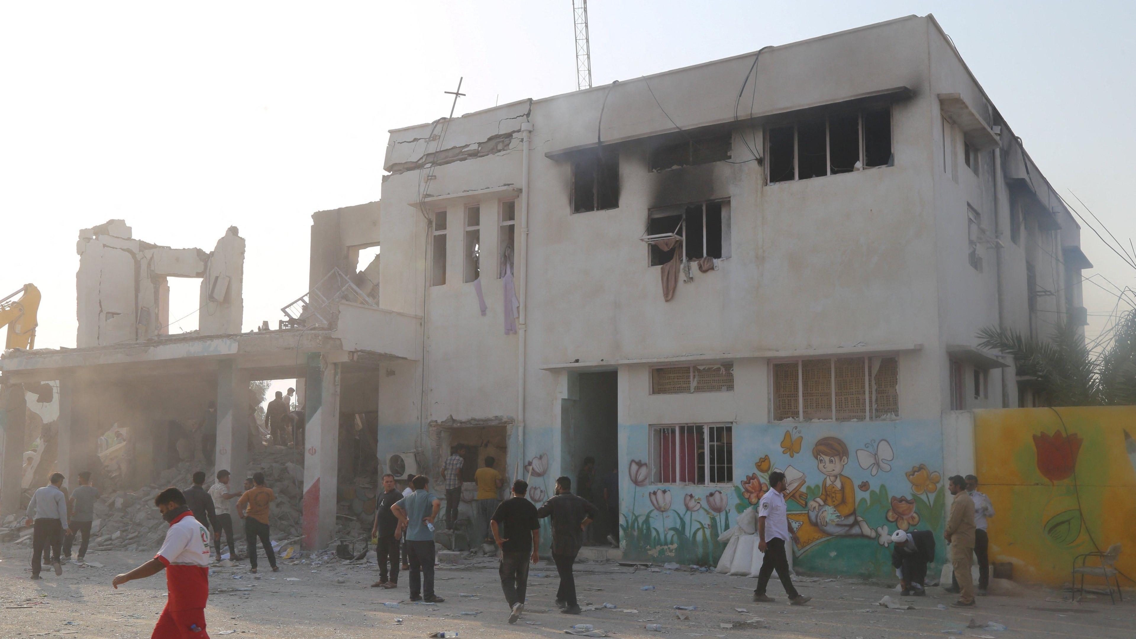 A still showing the aftermath of the strike on Minab. The exterior of the buidling is heavily damaged and people are seen outside inspecting it.