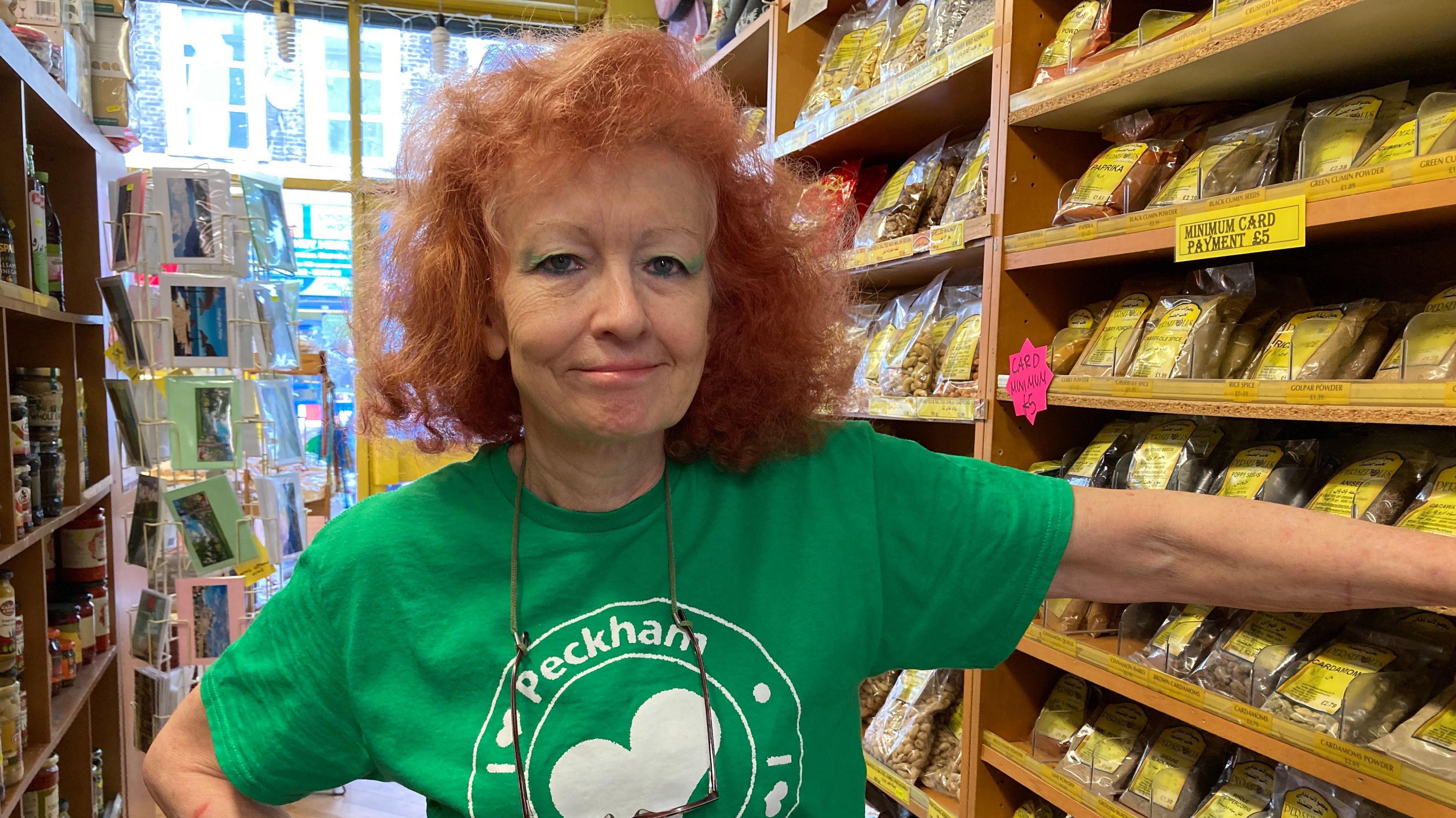 Sally Butcher in a green I love Peckham t-shirt. She stands inside her Middle-Eastern shop.