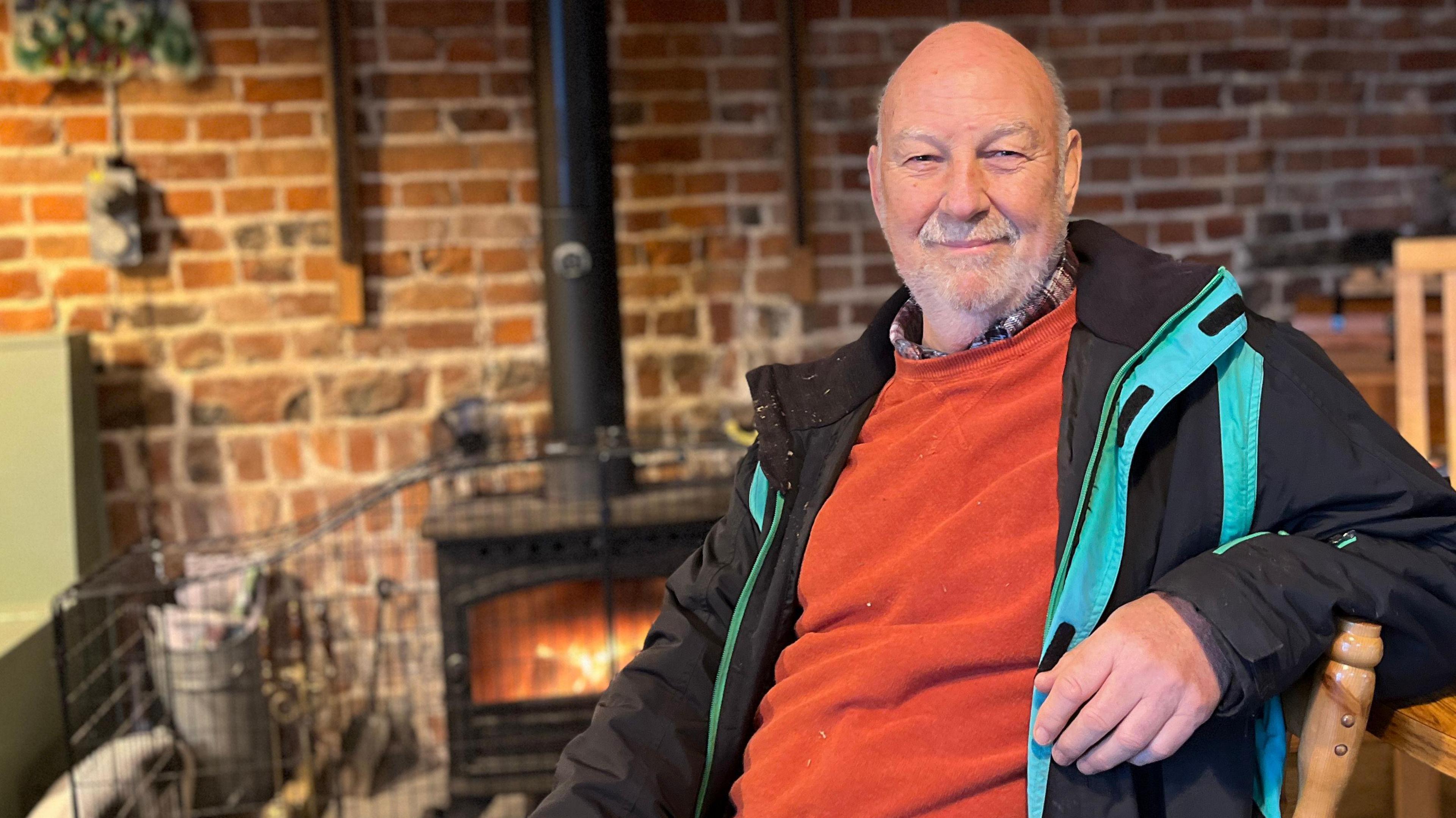 Geoff Stevens sits in front of a log burner in the Pathways farm café