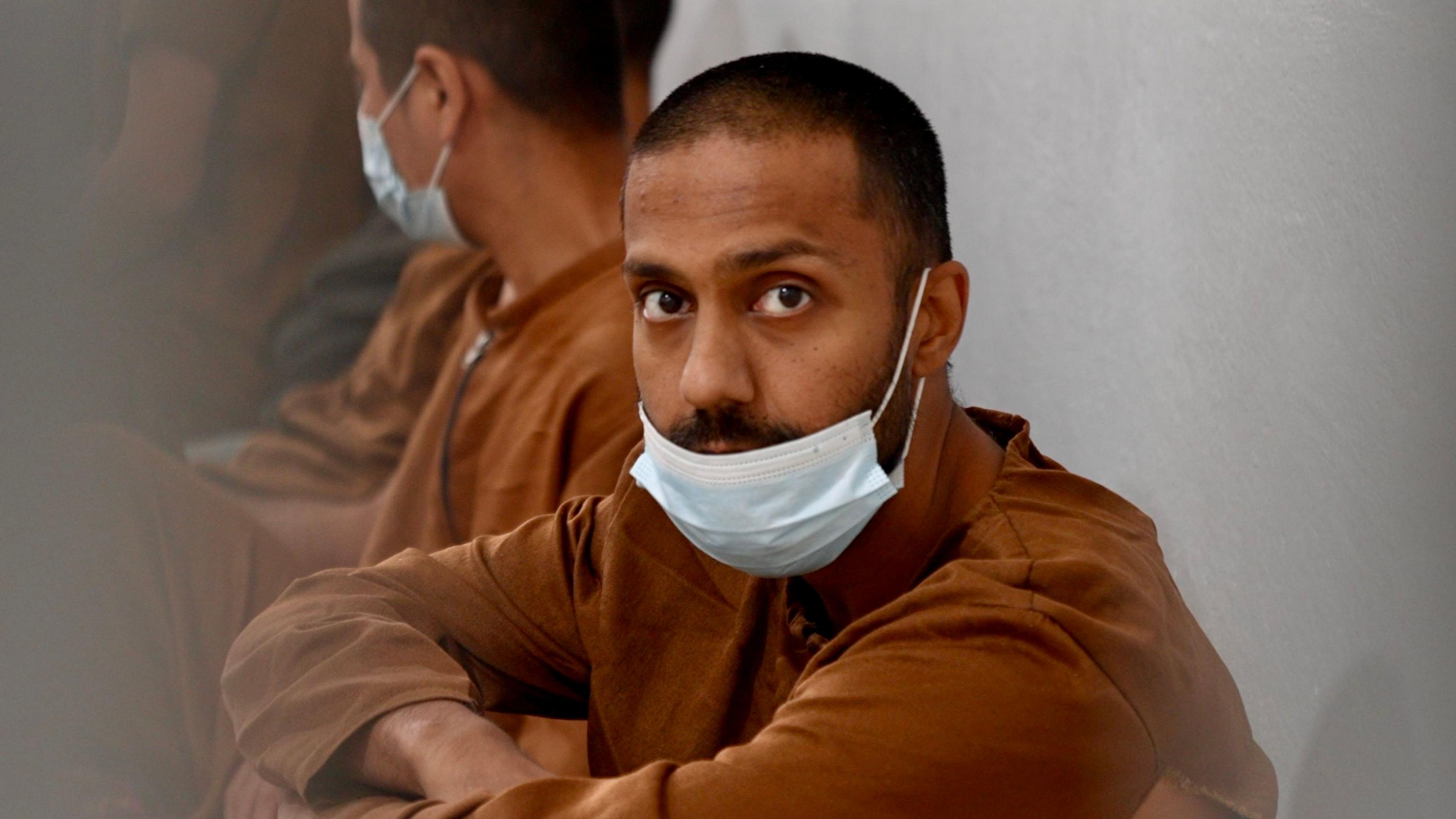 Hamza Parvez stares whilst wearing a mask and a dark brown top.