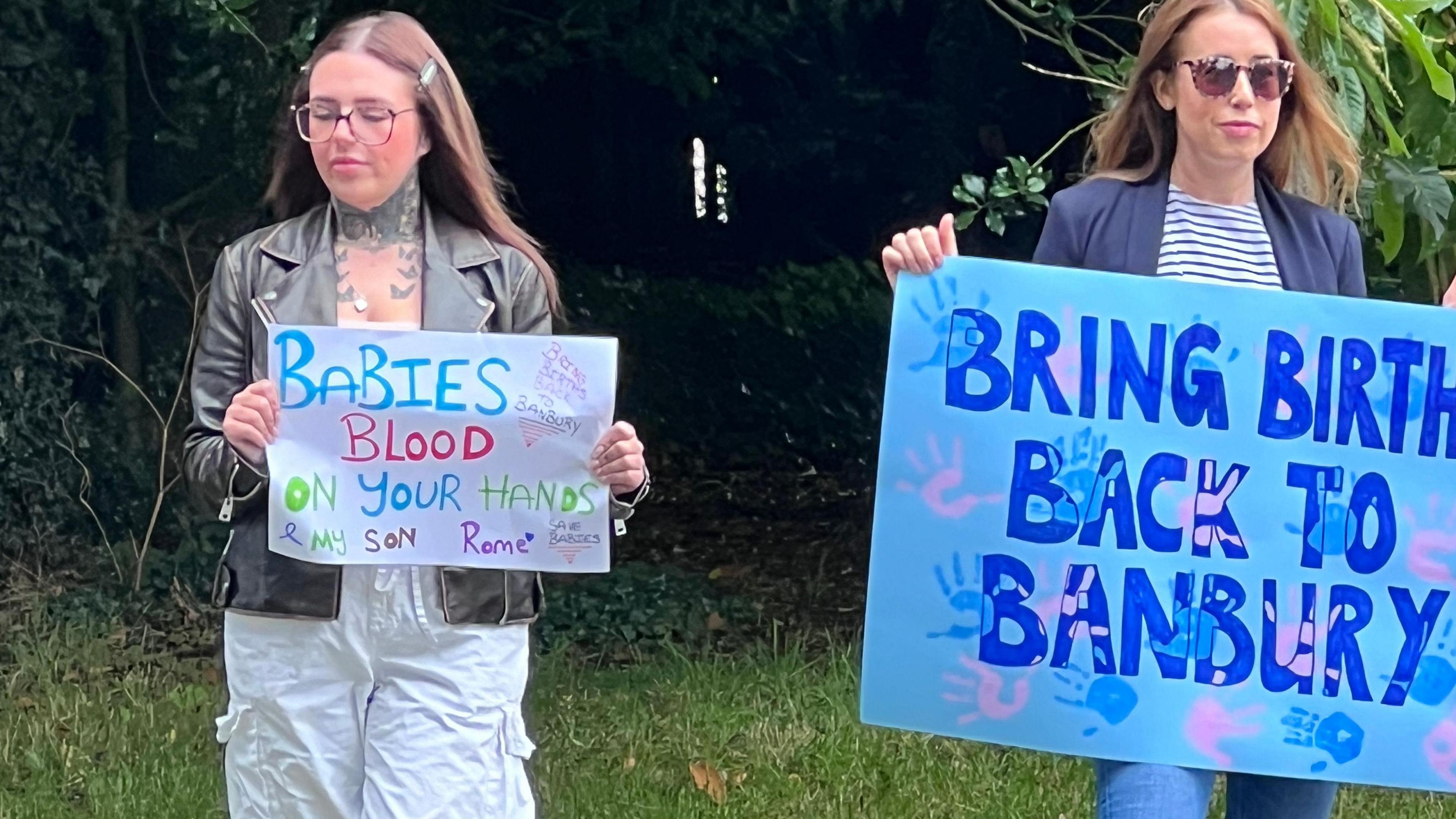 Two female protesters with placards by the side of the road. 