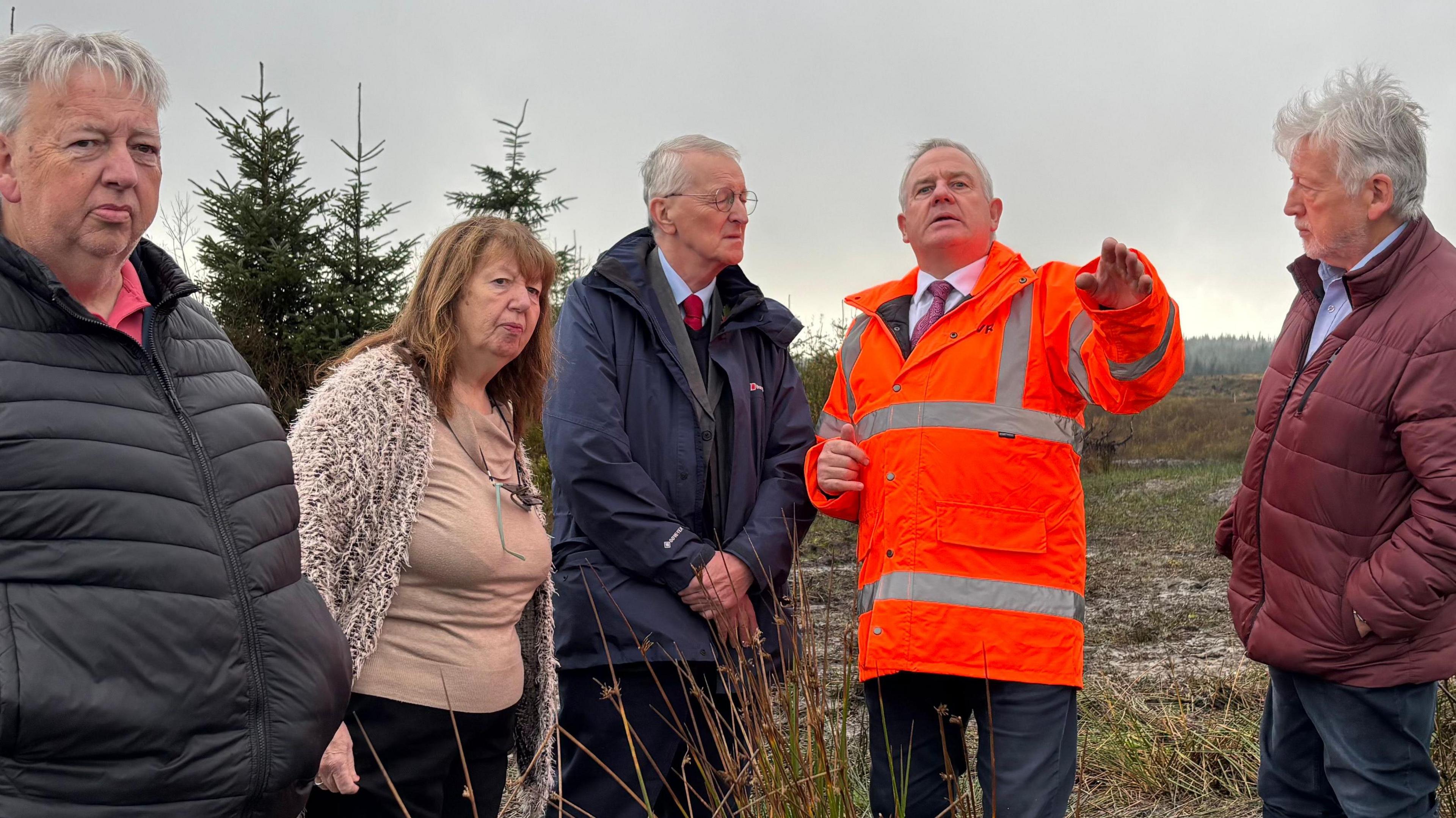 From left to right, a man, a woman and three men, including Northern Ireland Secretary of State Hilary Benn, stand in a field. 