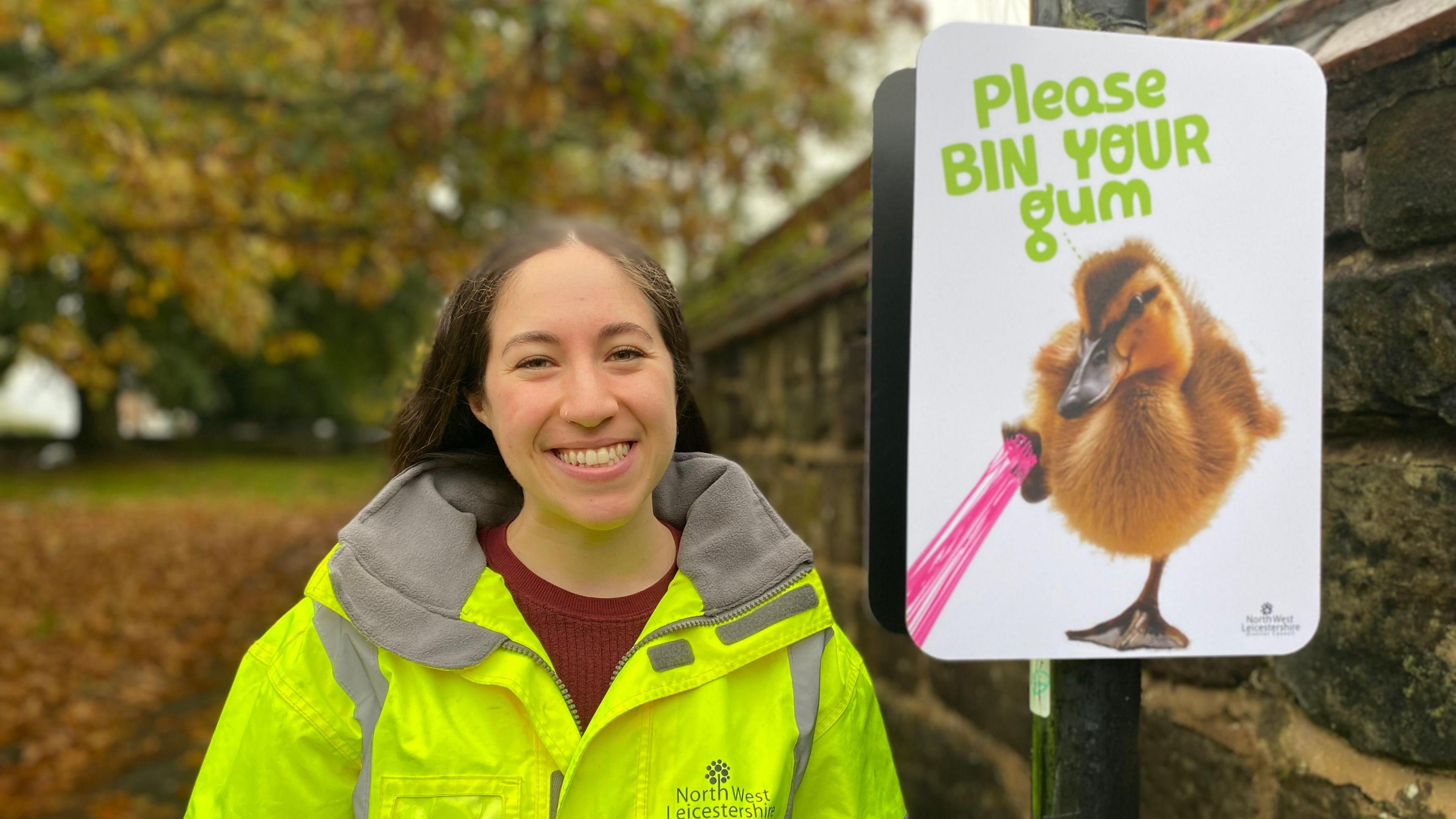 Lily Walker in hi-vis jacket underneath a poster that says: "Please bin your gum"