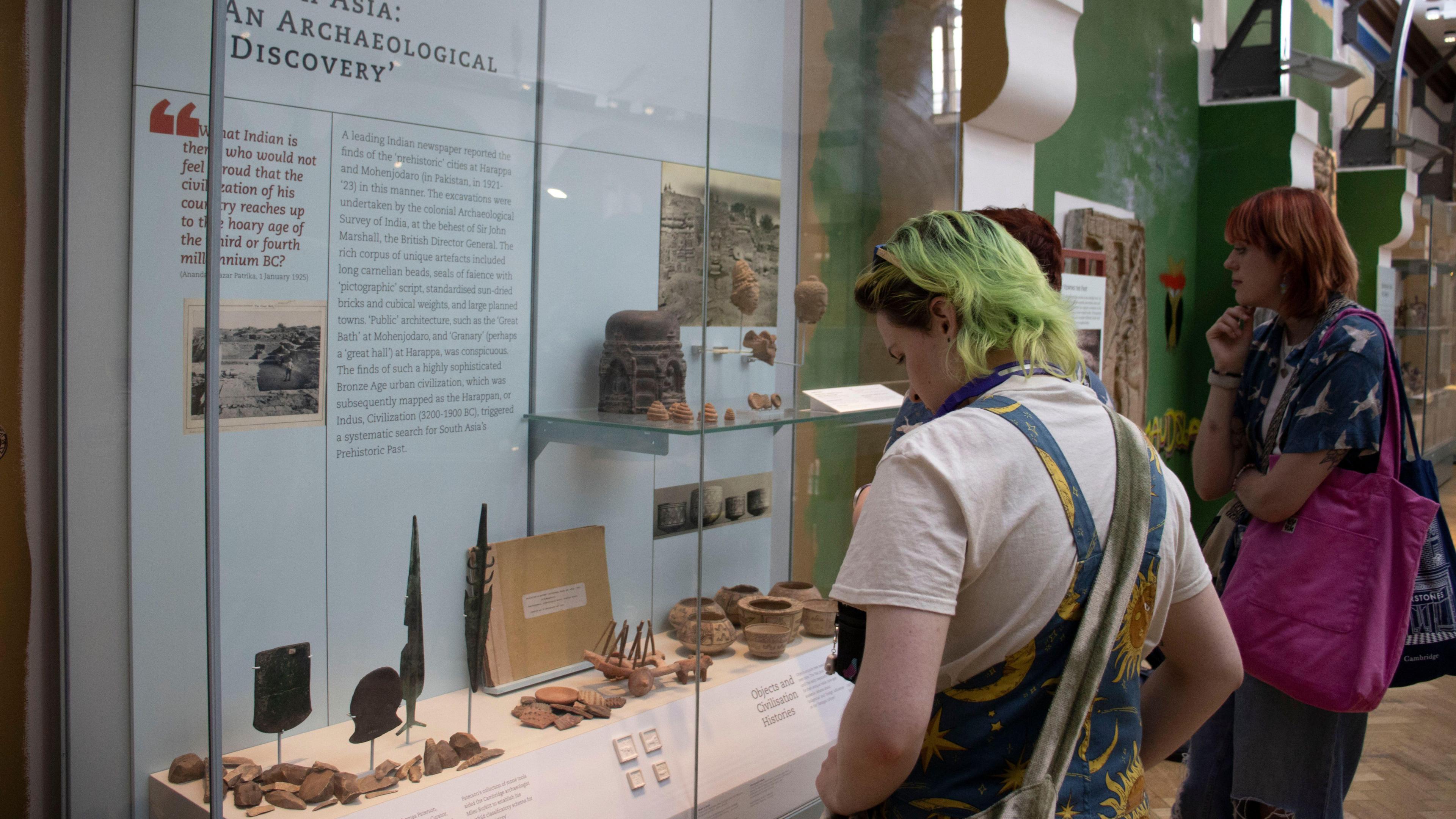 Two people, one person with colourful hair, looking at displays at the Museum of Archaeology and Anthropology.