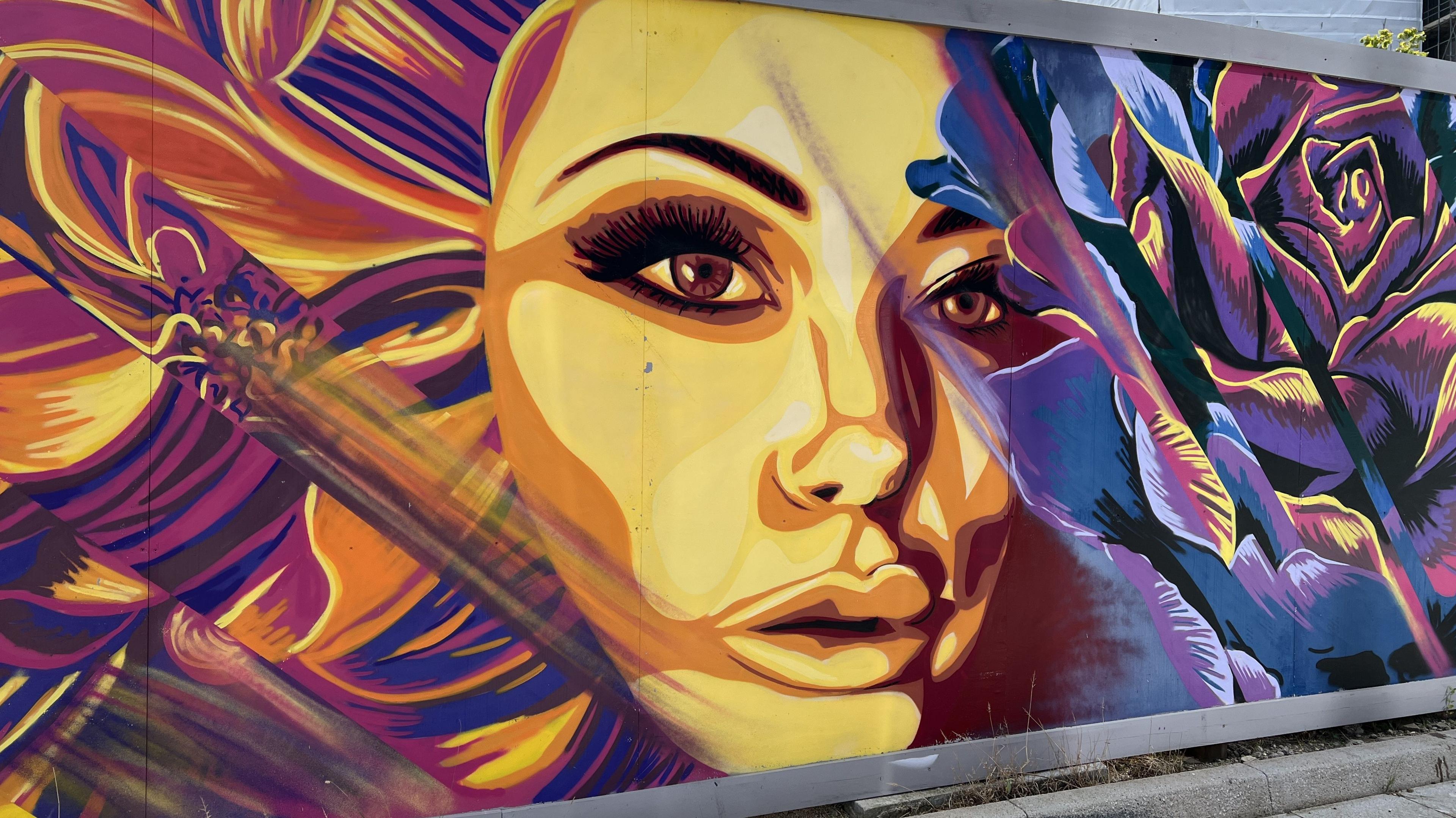 Large mural across a Swindon wall of a woman's face surrounded by different coloured flowers