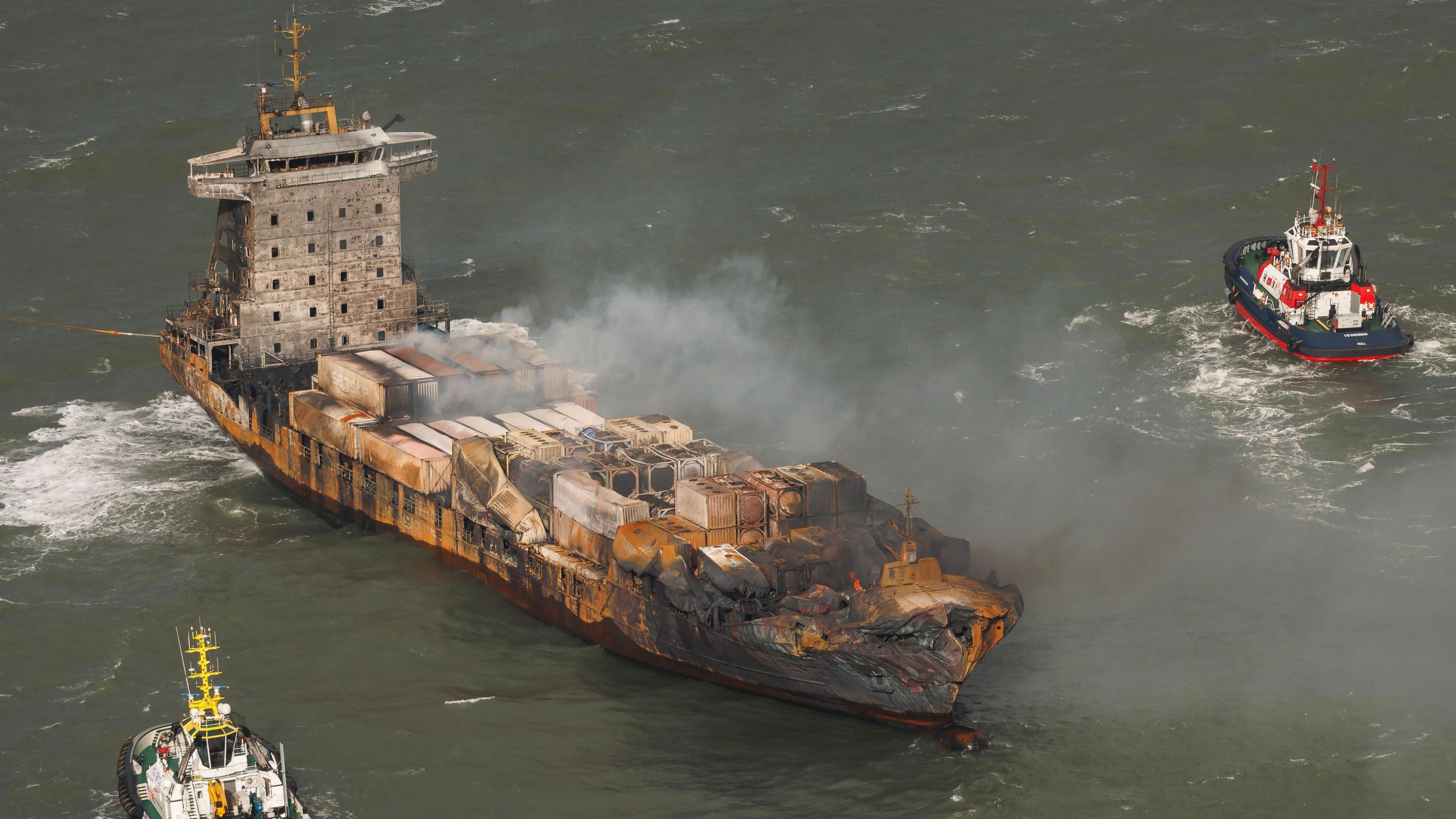 An aerial view of smoke billowing from the Solong cargo ship as it is flanked by two tug boats