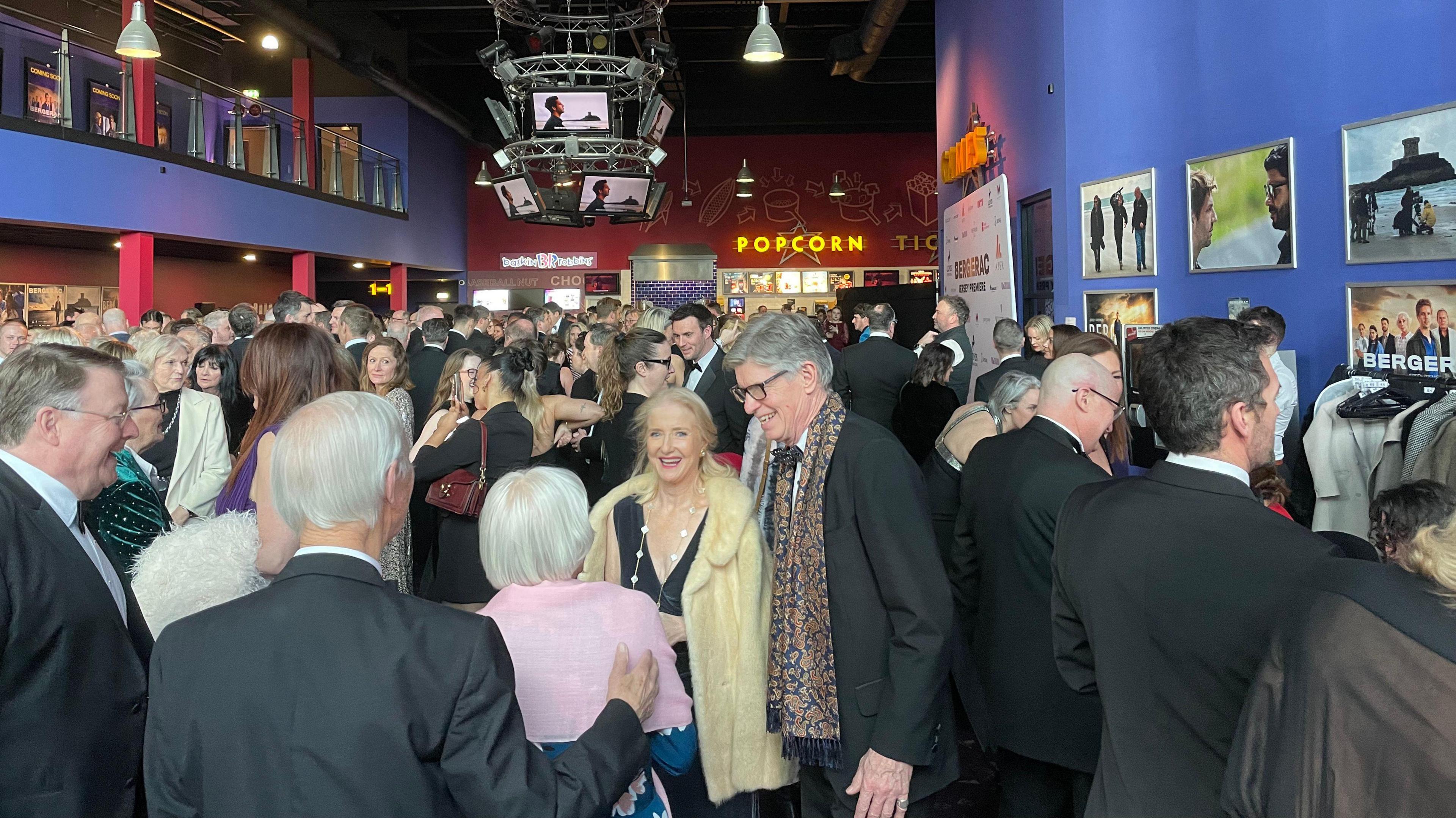 The event in the cinema is packed with smartly dressed people. There are photos from the TV shoot on the wall.