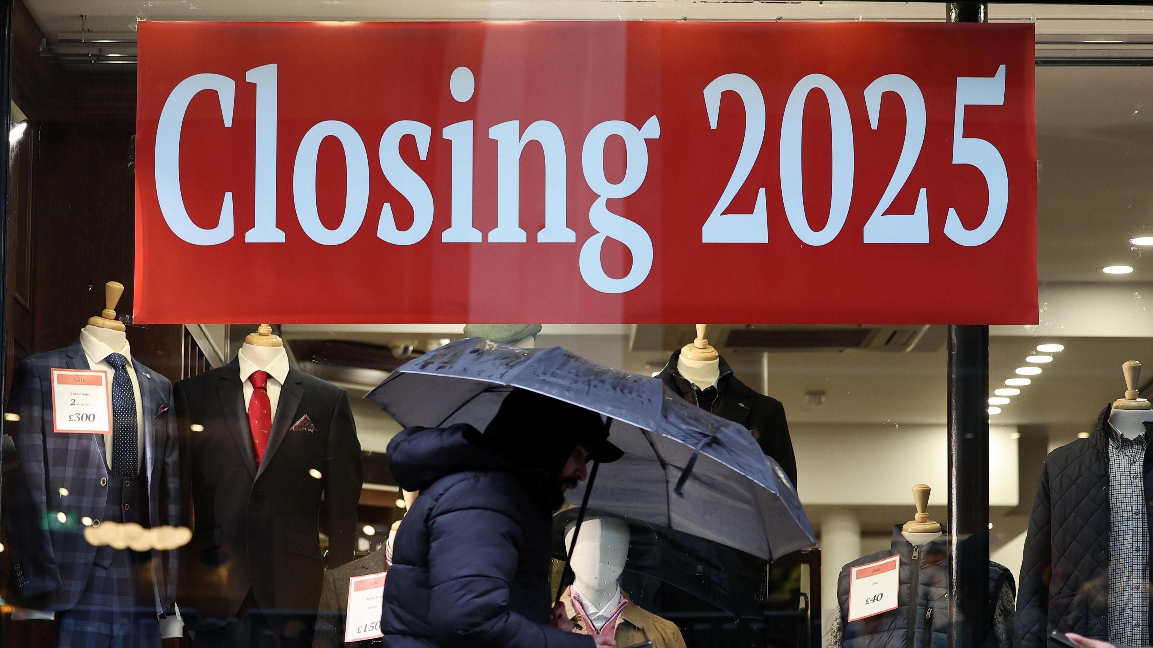 Person walks past a 'Closing 2025' sign in front of a shop