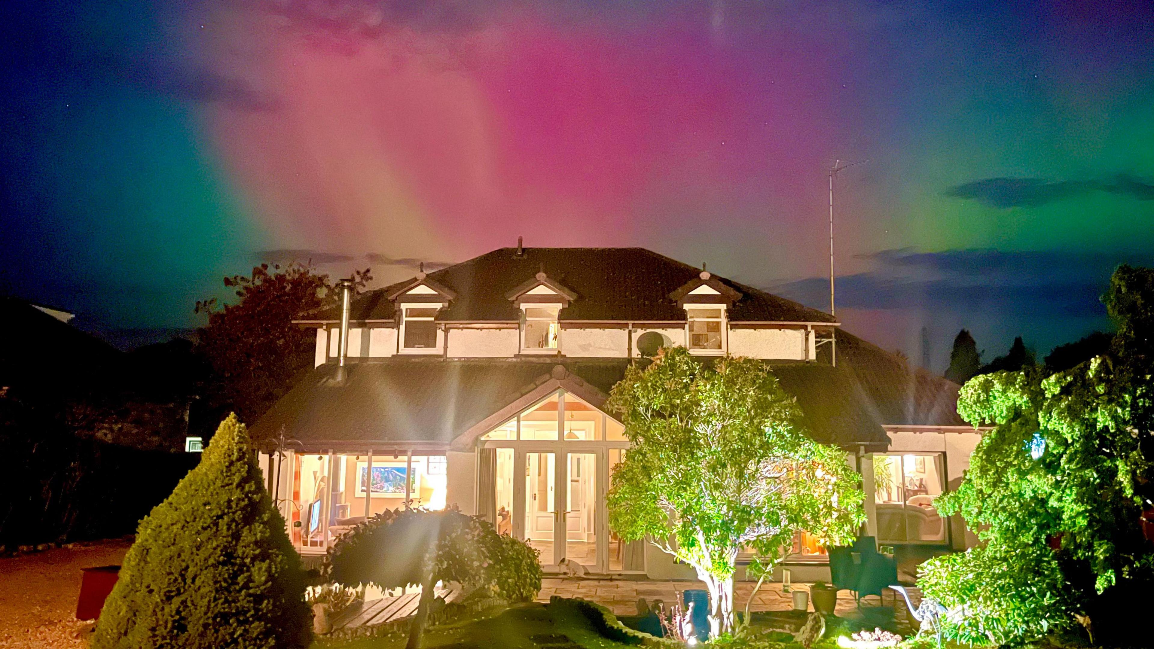 Colourful northern lights beam down on a house.