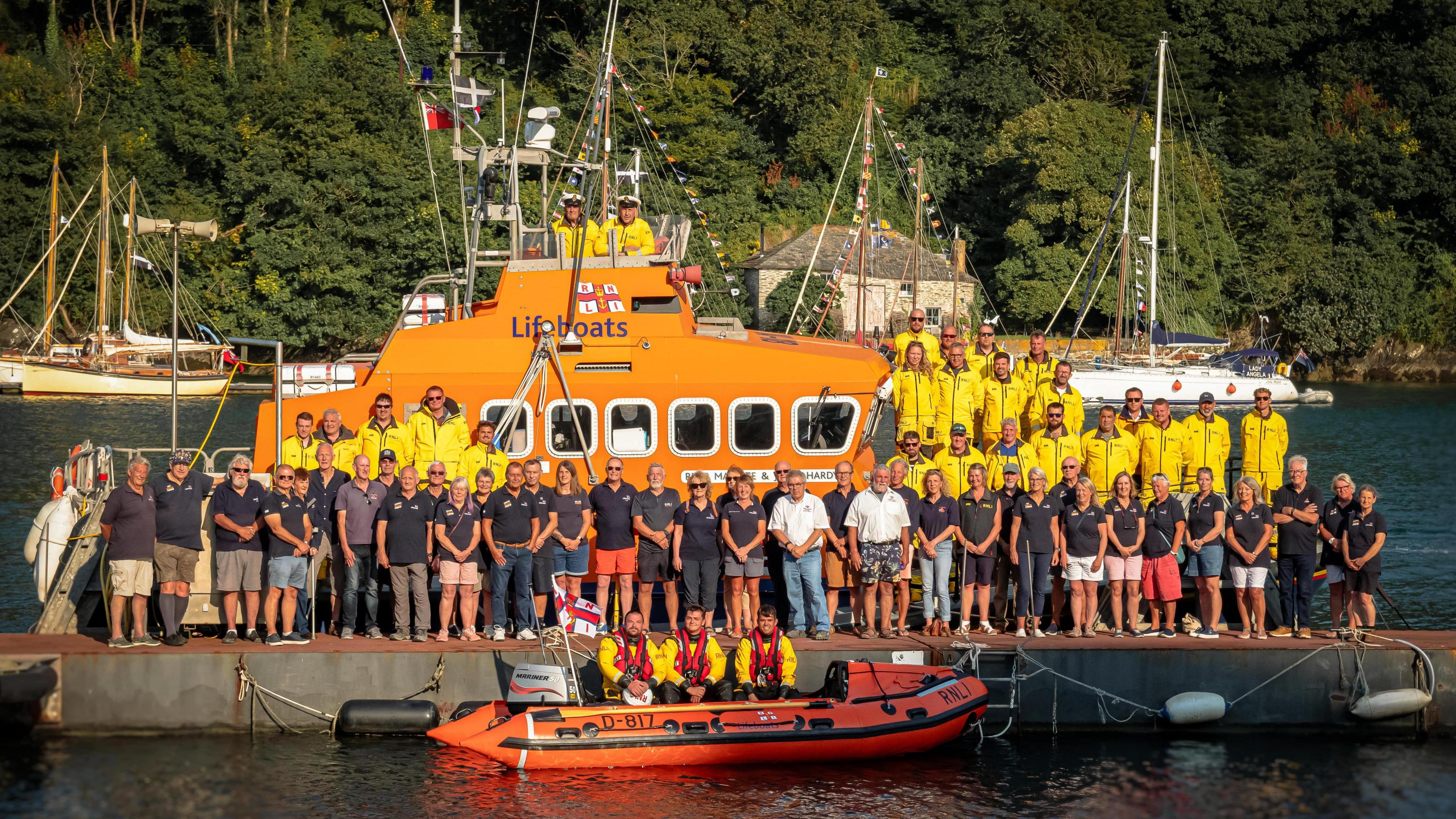 Fowey's Trent lifeboat with the whole RNLI team of station volunteers lined up on and around the vessel with an inshore RIB in front.