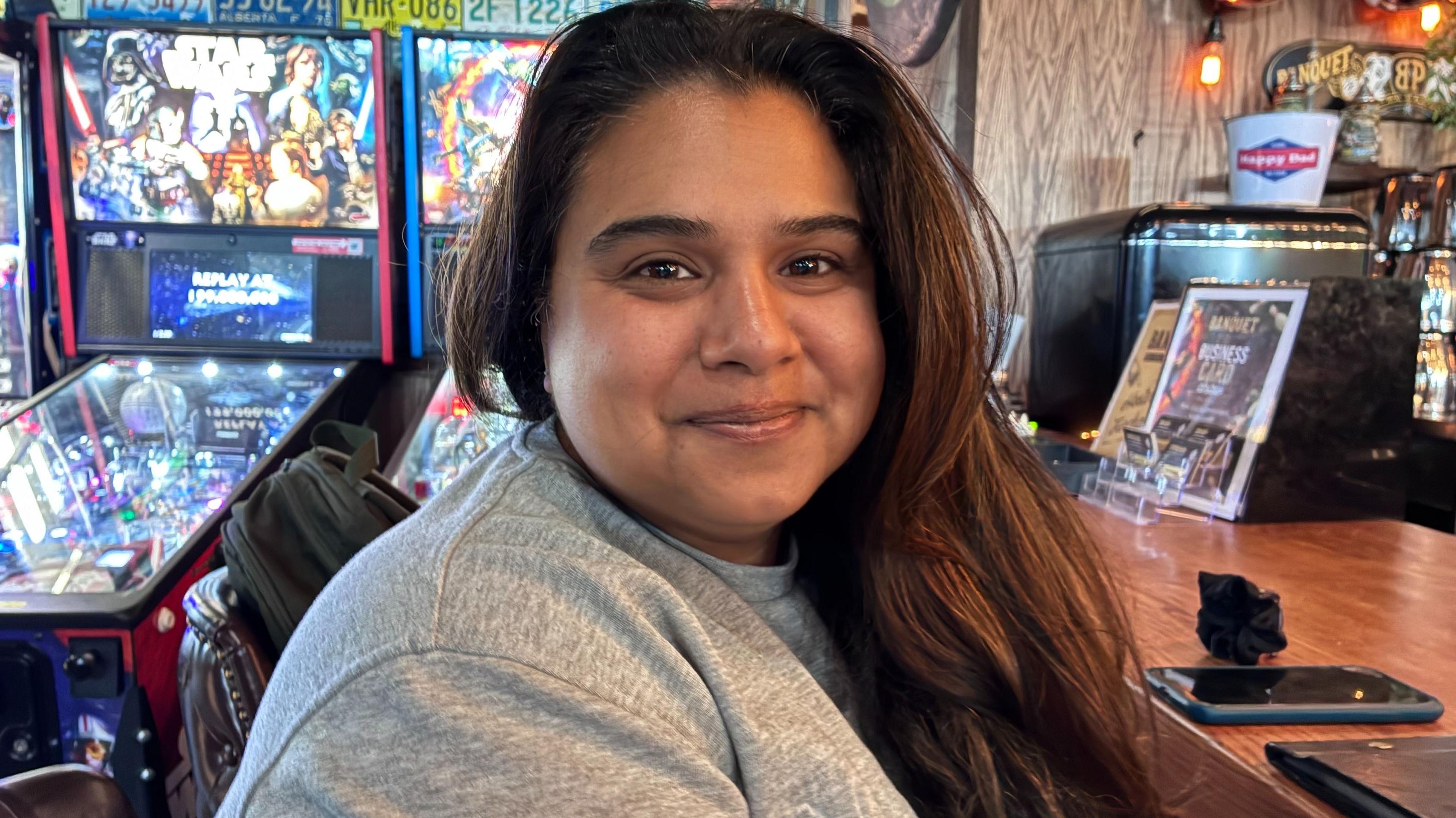 Zeileen Reardon, wearing a grey sweatshirt, with her long dark hair loose, smiles at the camera. 