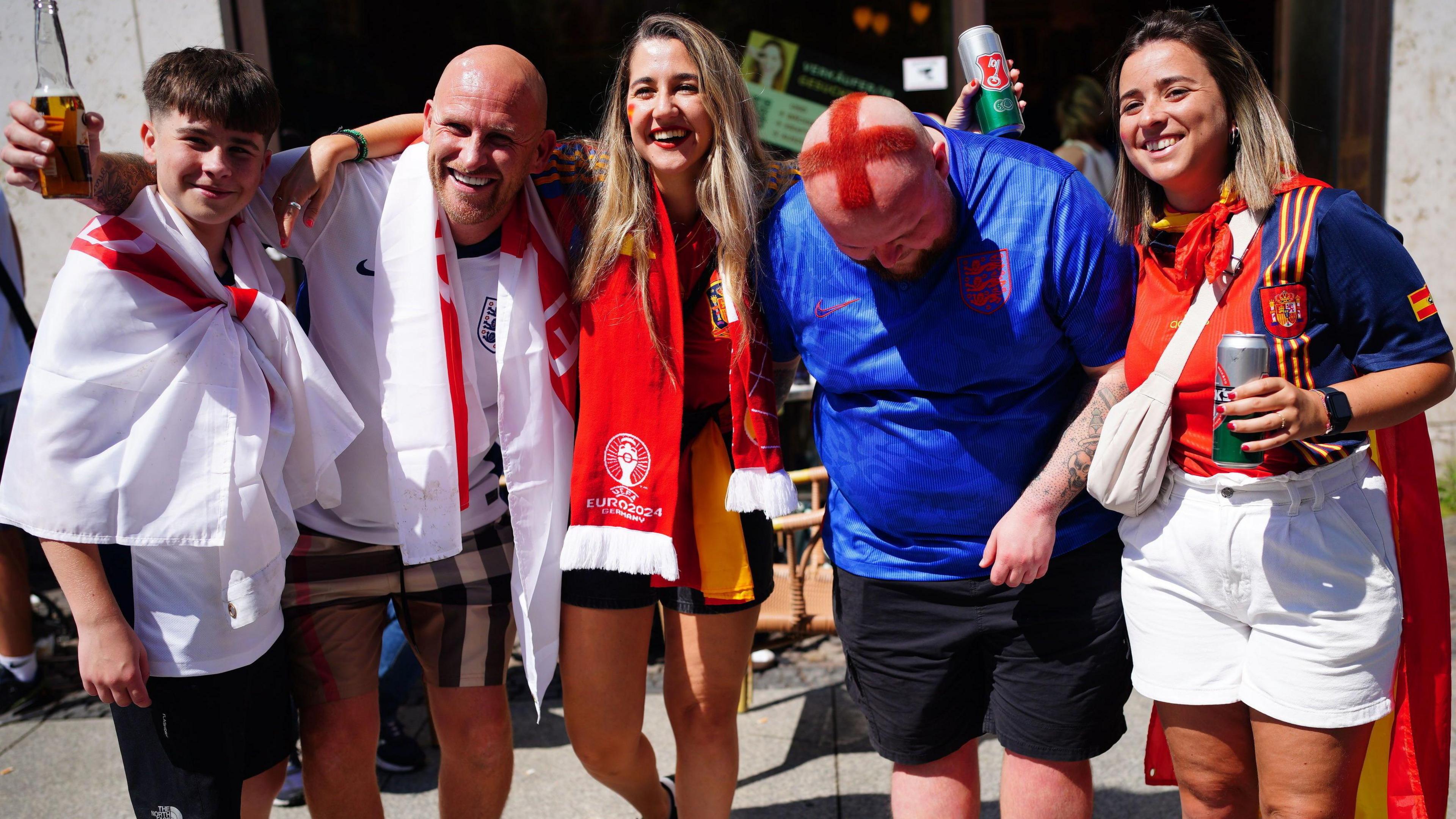 Four England fans smile for the camera, with one bowing his head to show it shaved and dyed red to be a red cross.