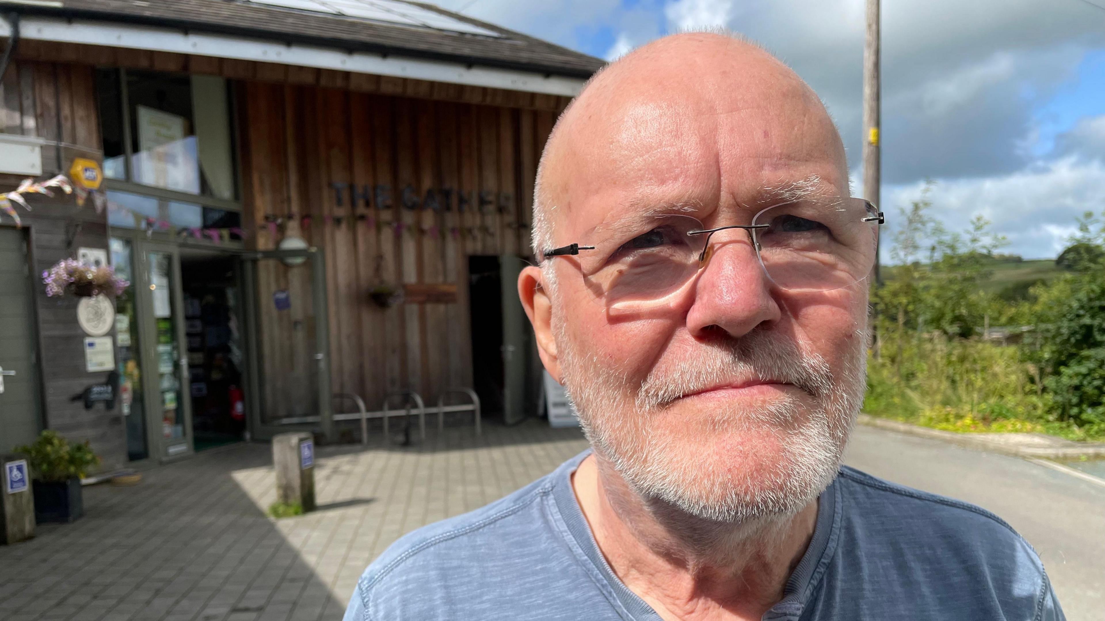 A man outside The Gather building, with a bald head and white beard, wearing glasses.