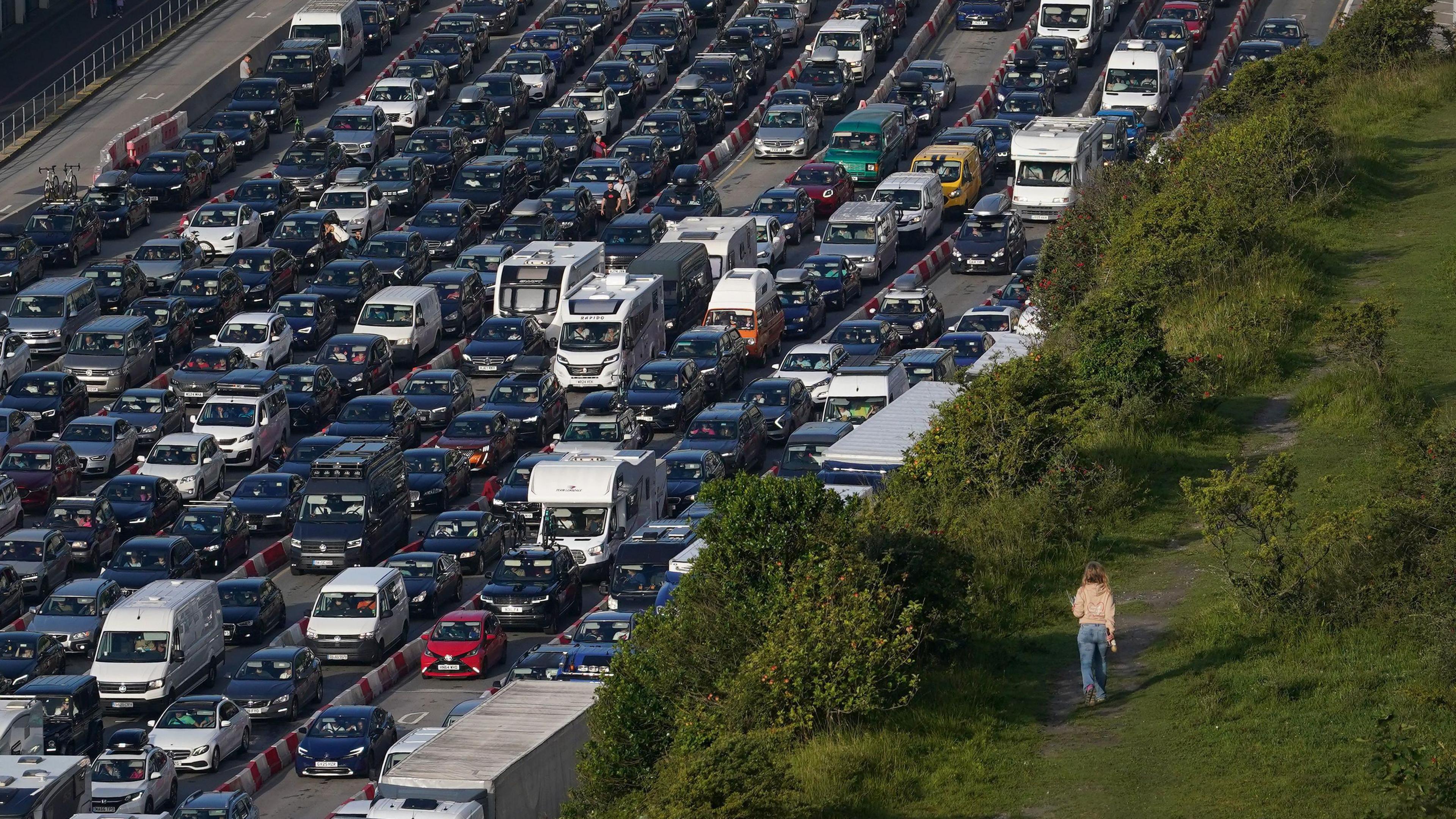 A lady walks across the cliffs while holiday and freight traffic queue to use the Port of Dover in Kent, as travellers make their way across the Channel for the summer holidays.