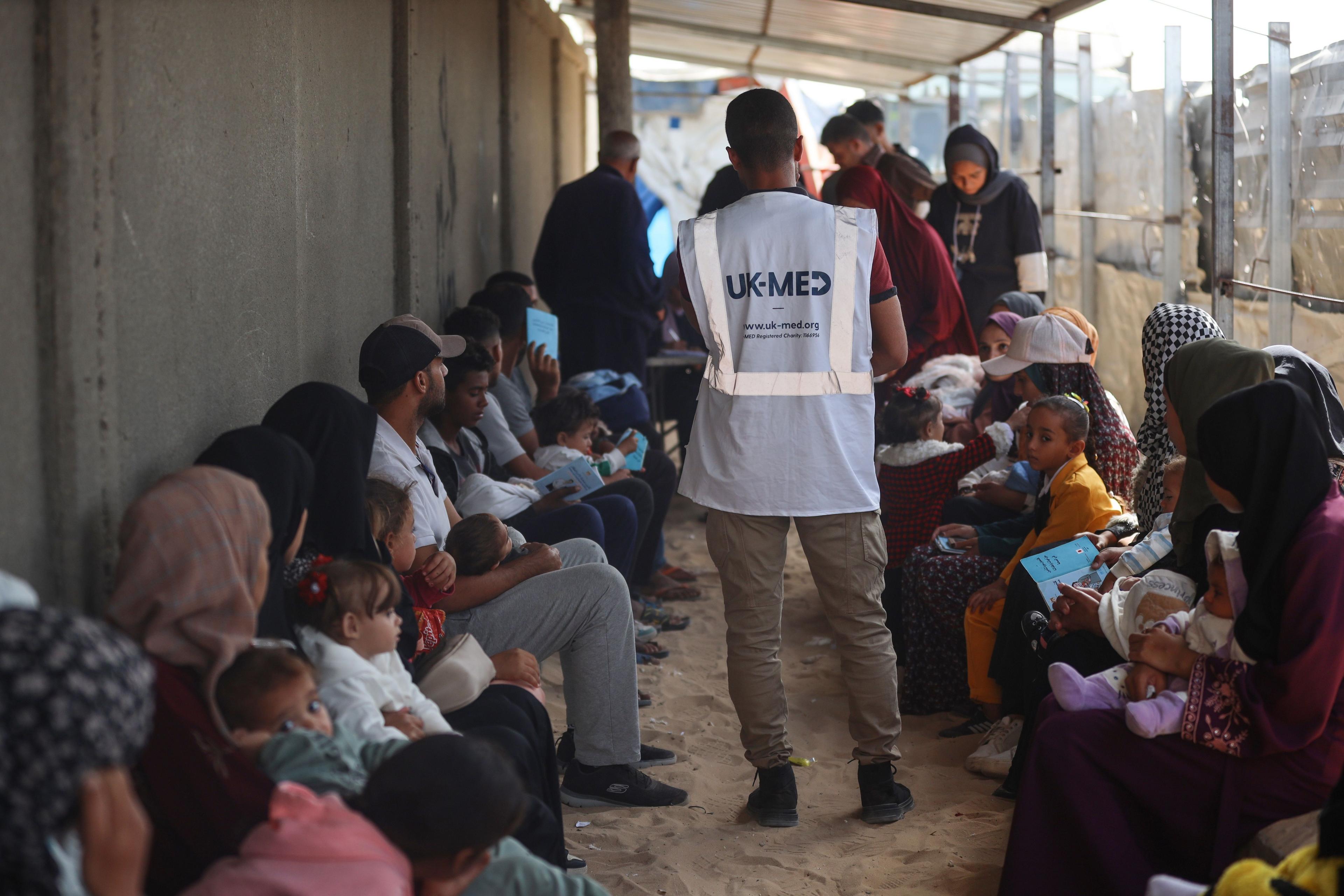 Adults and children sitting in a corridor, with a man bearing a UK-Med vest in the middle.