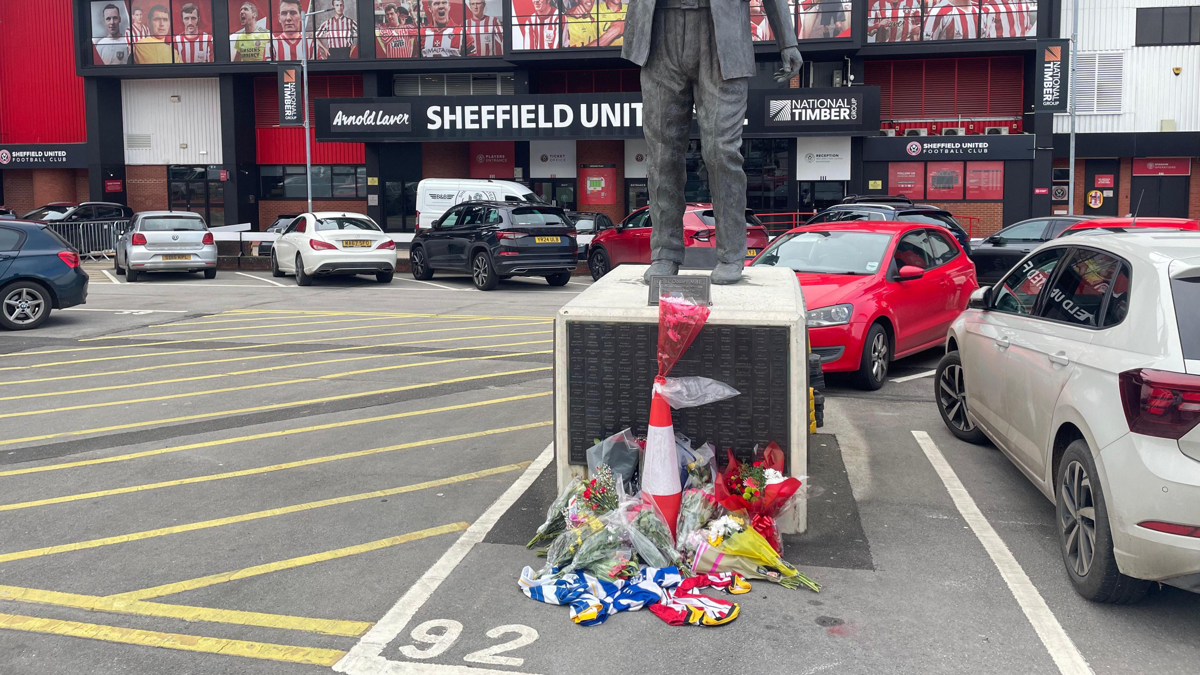 Floral tributes and t-shirts have been placed in front of a bronze statue outside the football stadium.