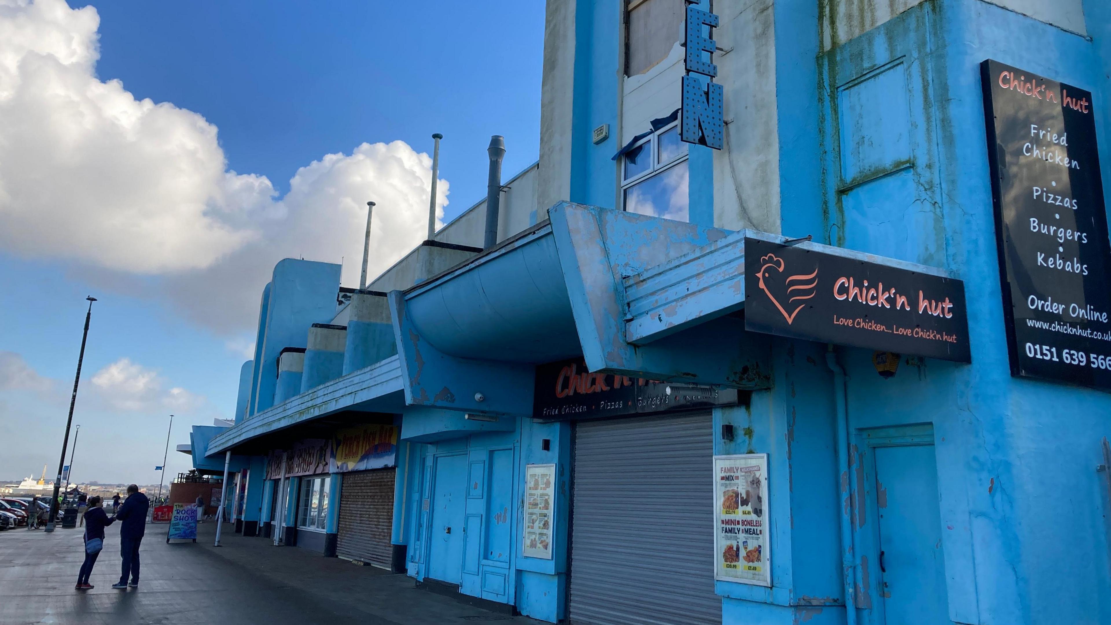 The light blue exterior of New Brighton's arcade. It is an Art Deco building built in the late 1930s. It has shutters down over the doors.