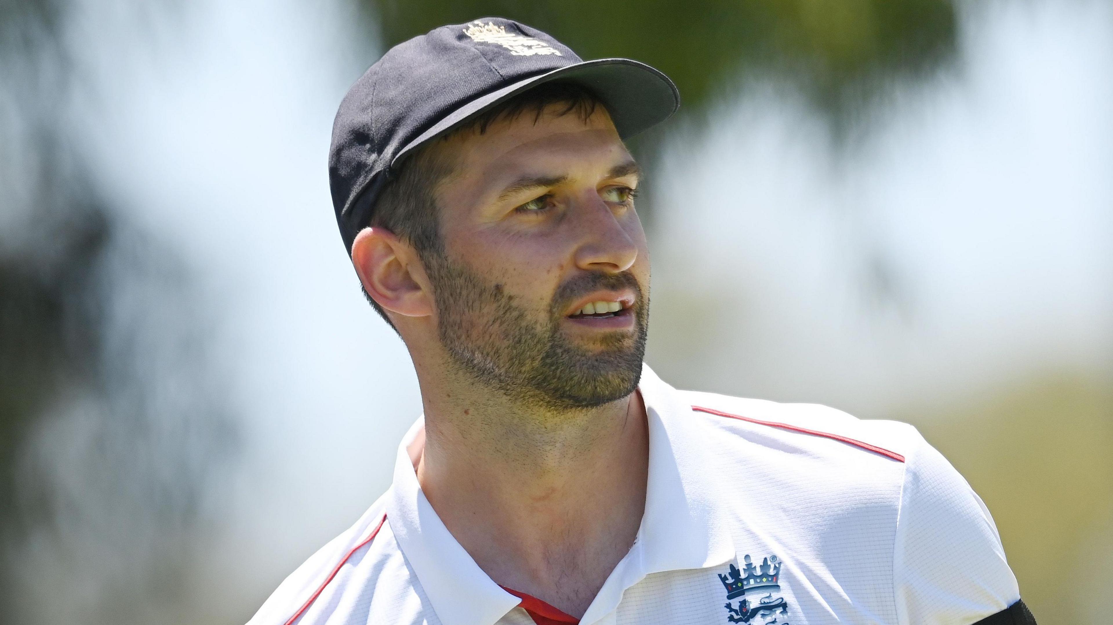 Mark Wood, wearing a blue England cap, looks to the side
