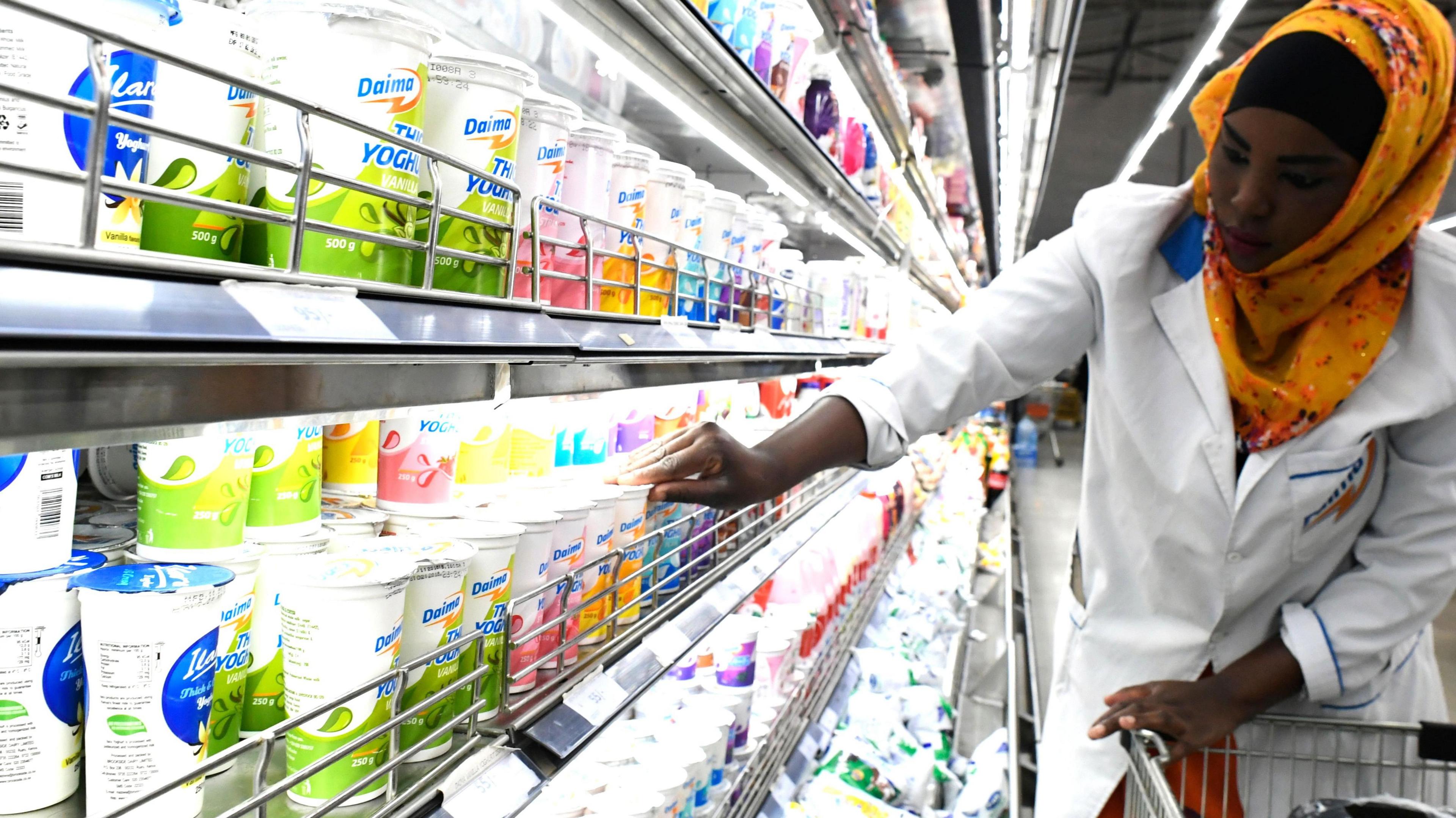 A shop assistant wearing an orange headscarf and a white coat fills the shelves with dairy products at supermarket in Nairobi, Kenya 