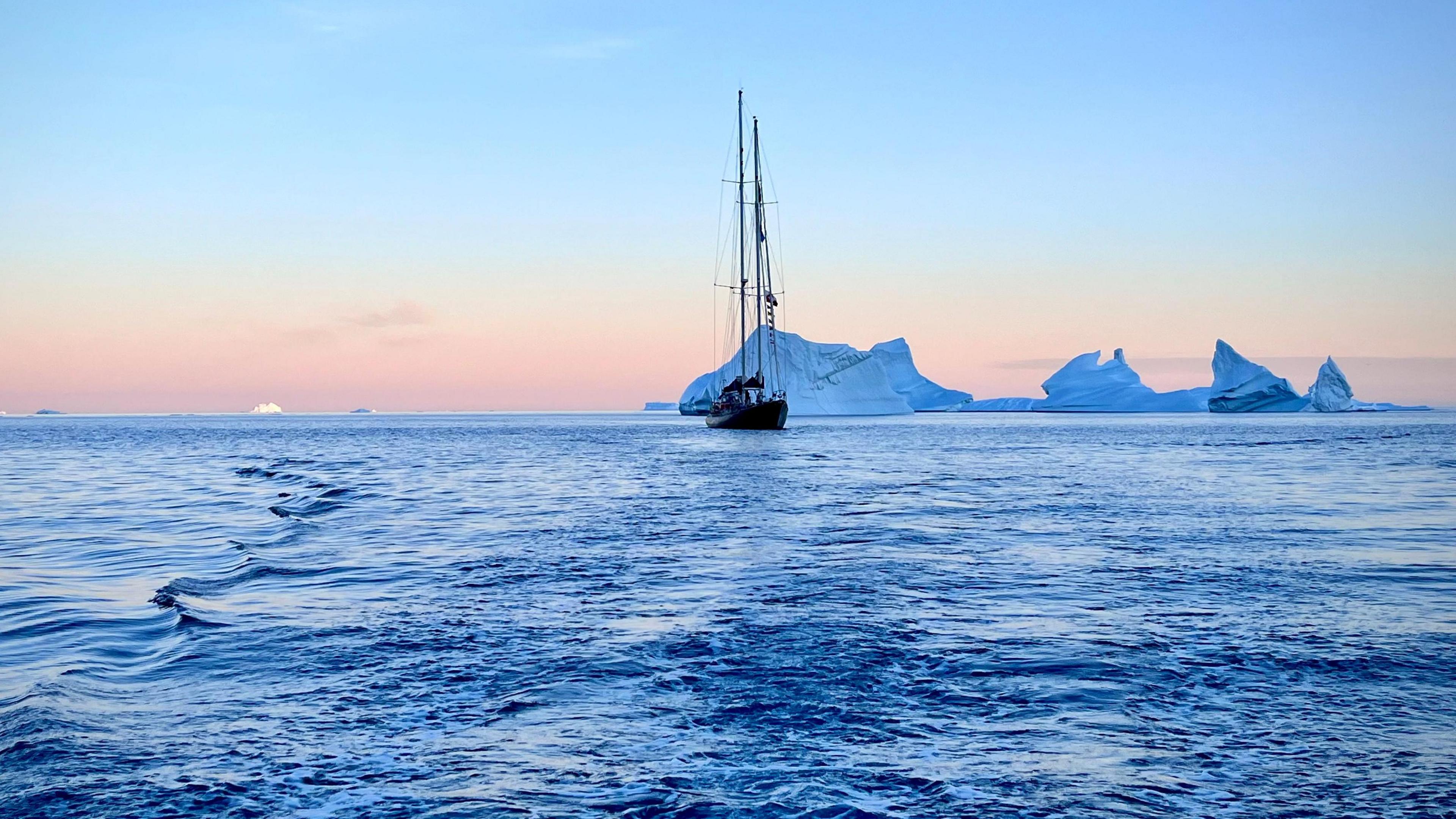 The Abel Tasman navigating through the waters of Disko Bay at sunset, with icebergs floating in the distance.