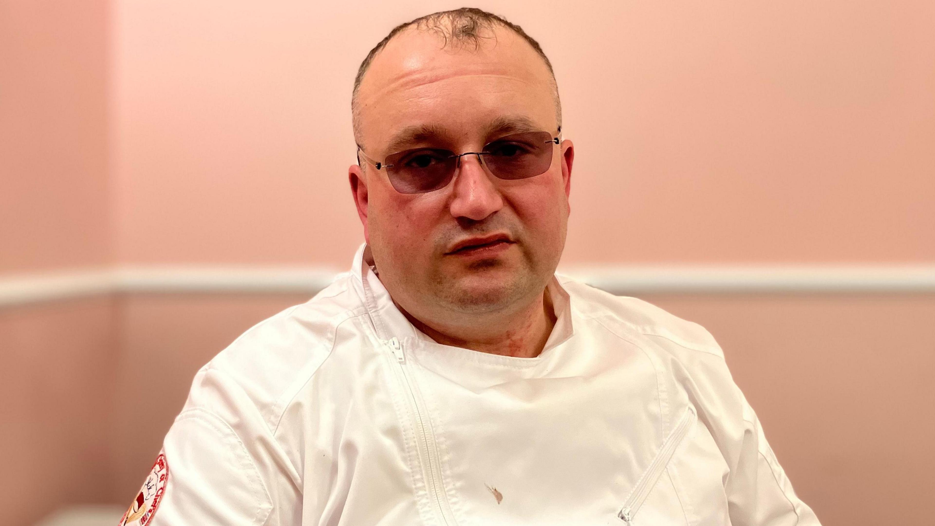 Maciej Bujakowski, who has short grey hair and tinted glasses. He is wearing chef whites in the photo.