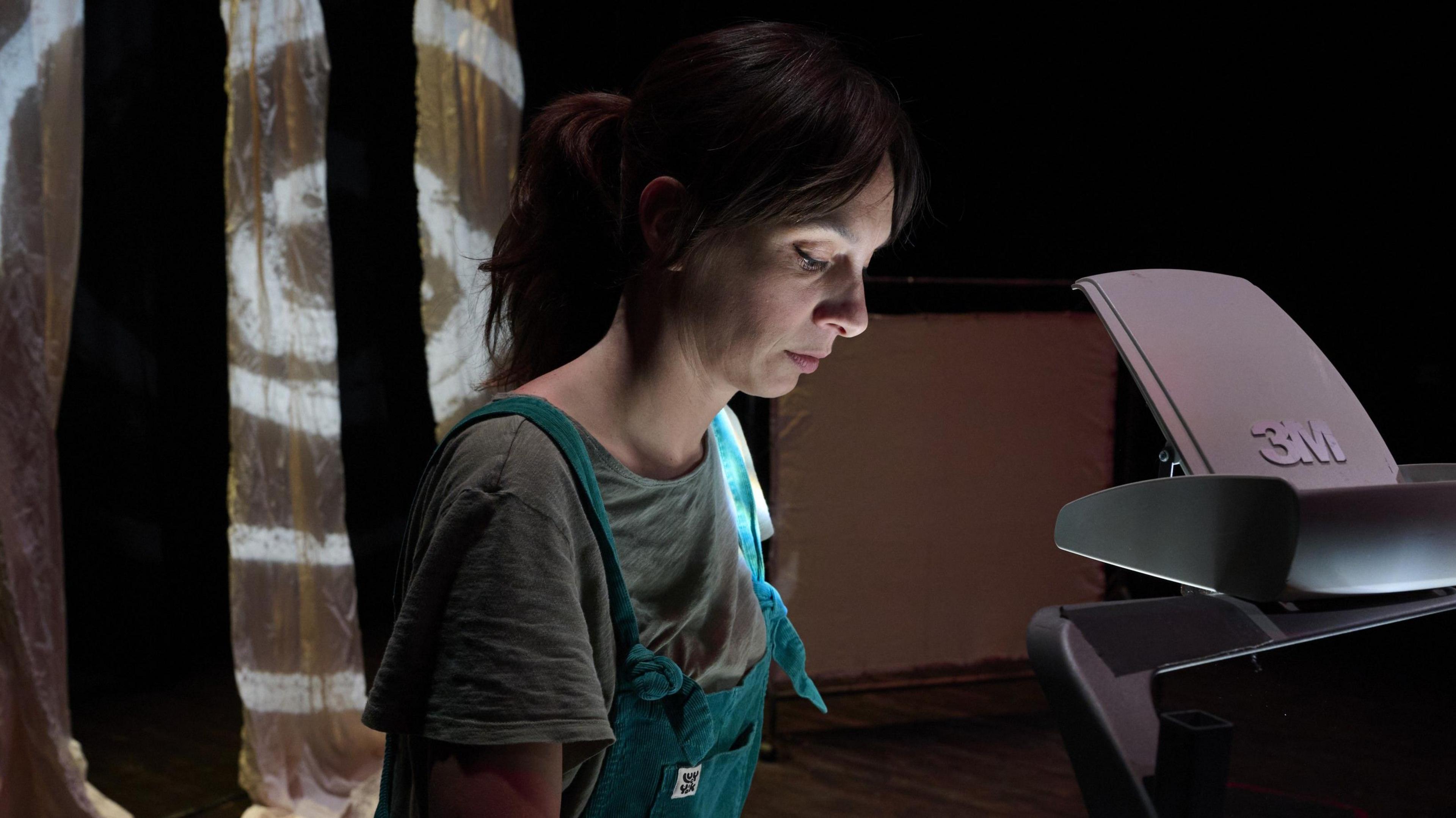 Ms Whiting looks down at an overhead projector. Her dark hair has been tied up behind her head.