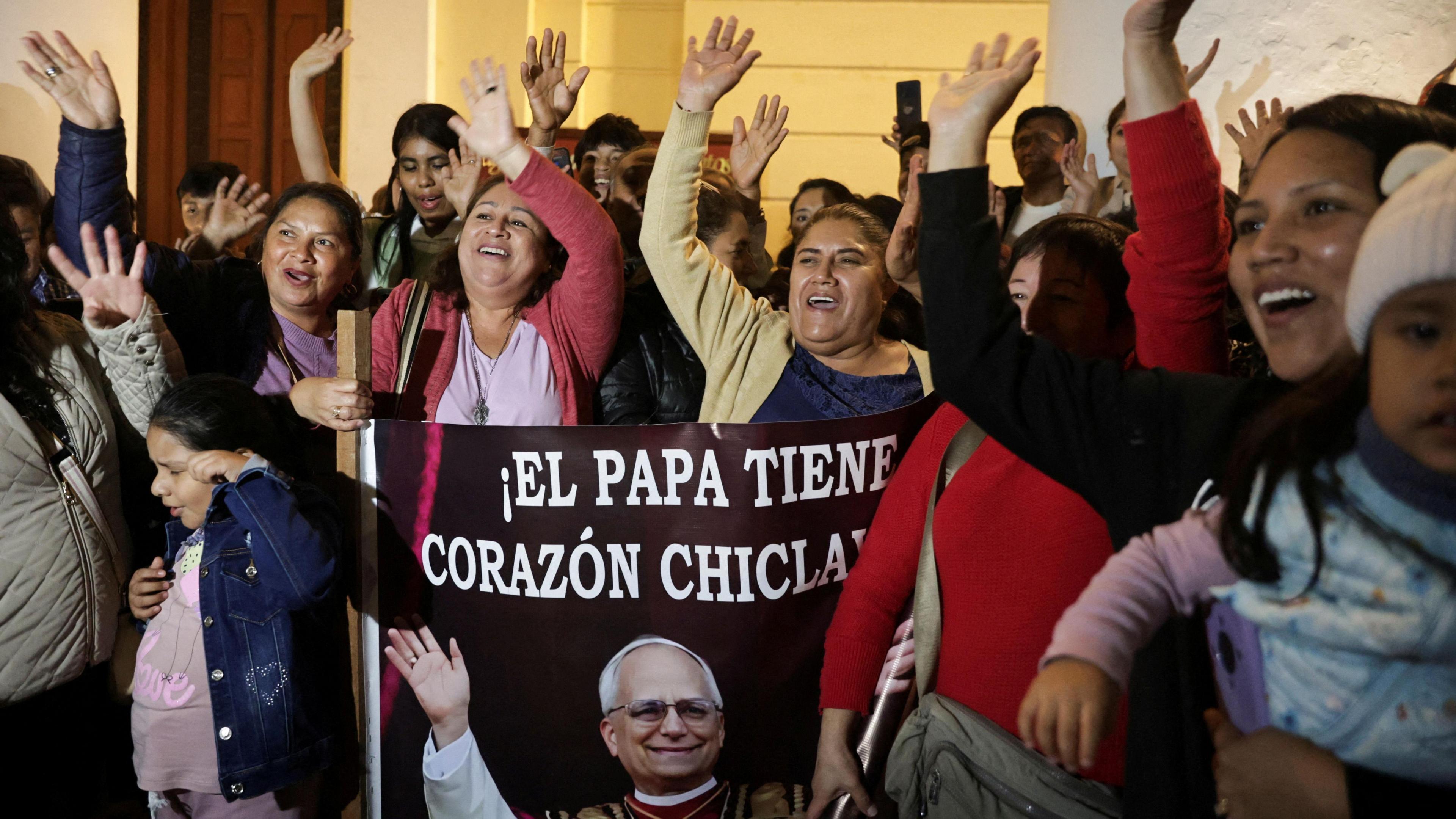A group of mainly women cheer with their hands in the air and hold a banner of Pope Louis XIV