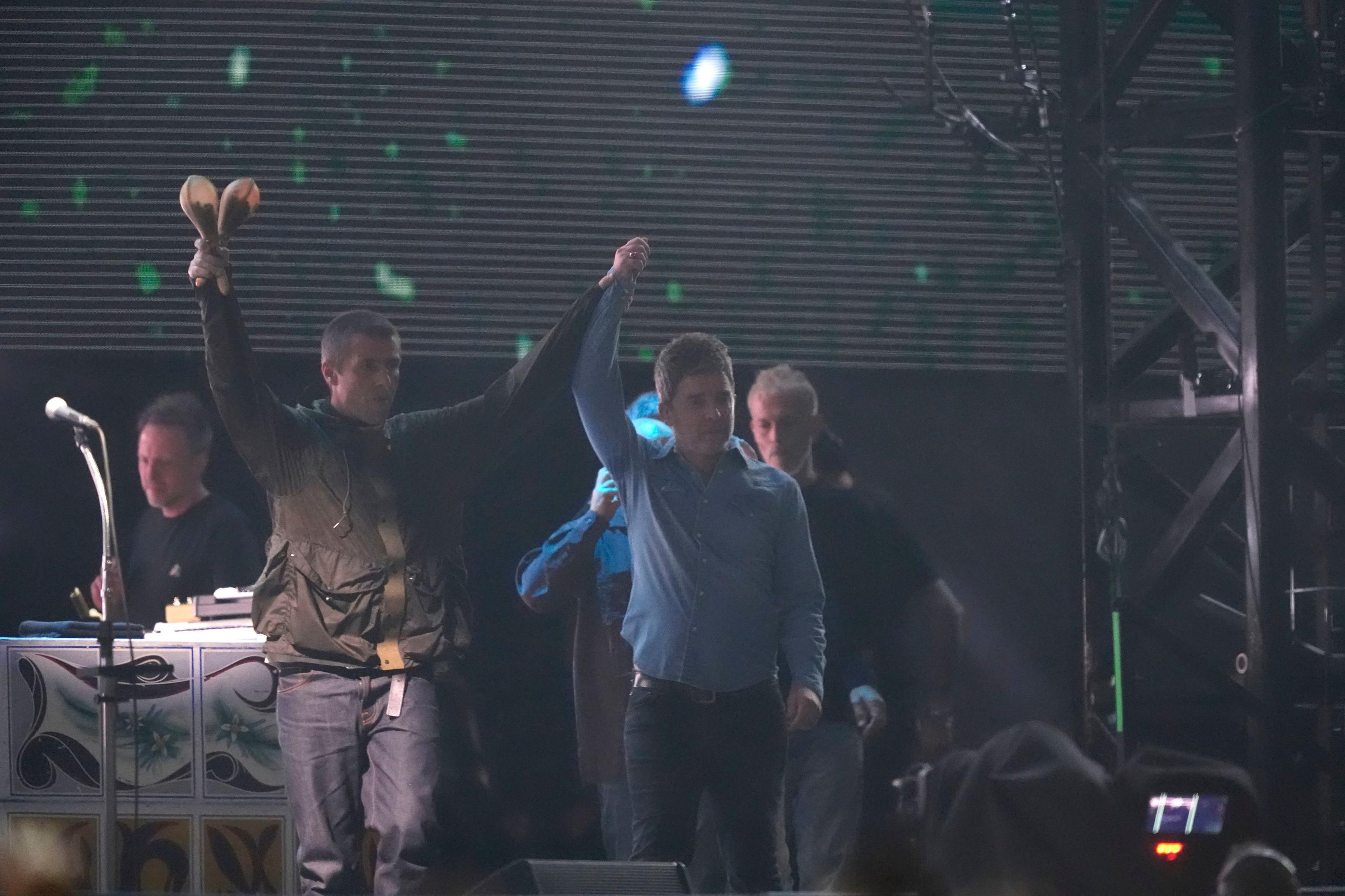 Liam and Noel Gallagher raise their hands in celebration during a show at their 2025 reunion tour