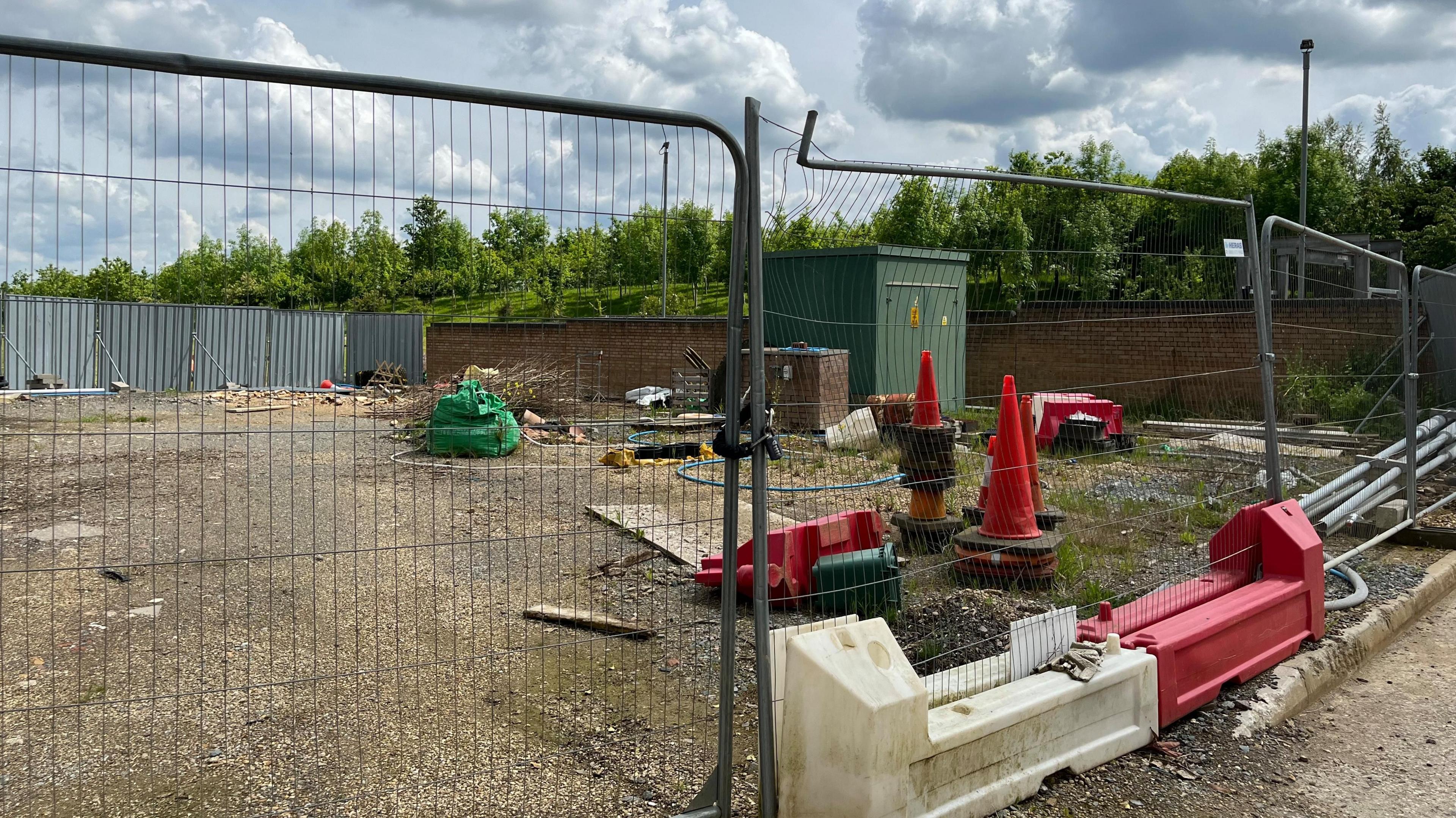 Metal fencing around rubble and cones with green trees surrounding it