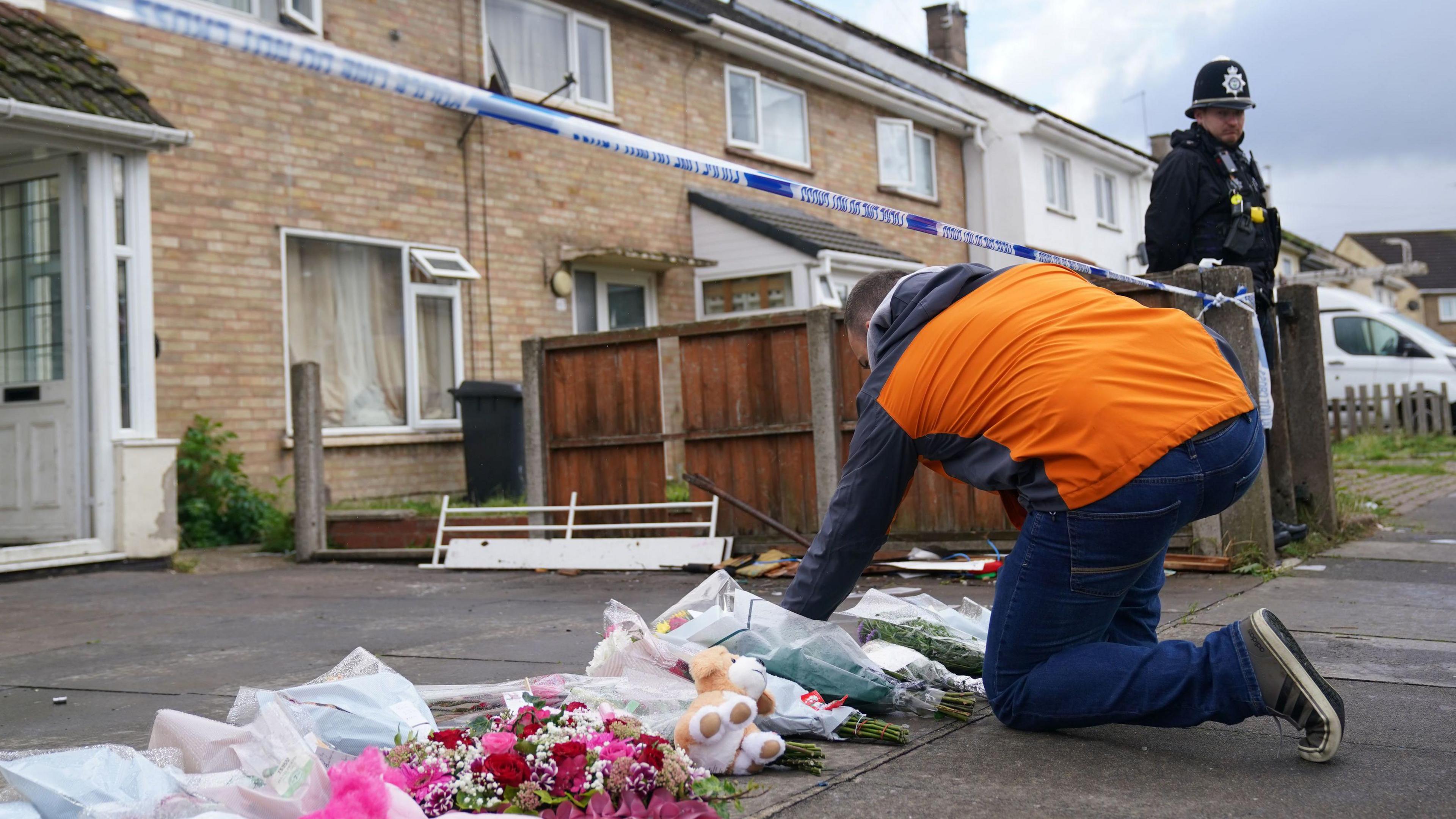 A man in an orange coat leaving a floral tribute outside the property on Bedale Drive, Leicester, where Chamiah Brindley died after a house fire.