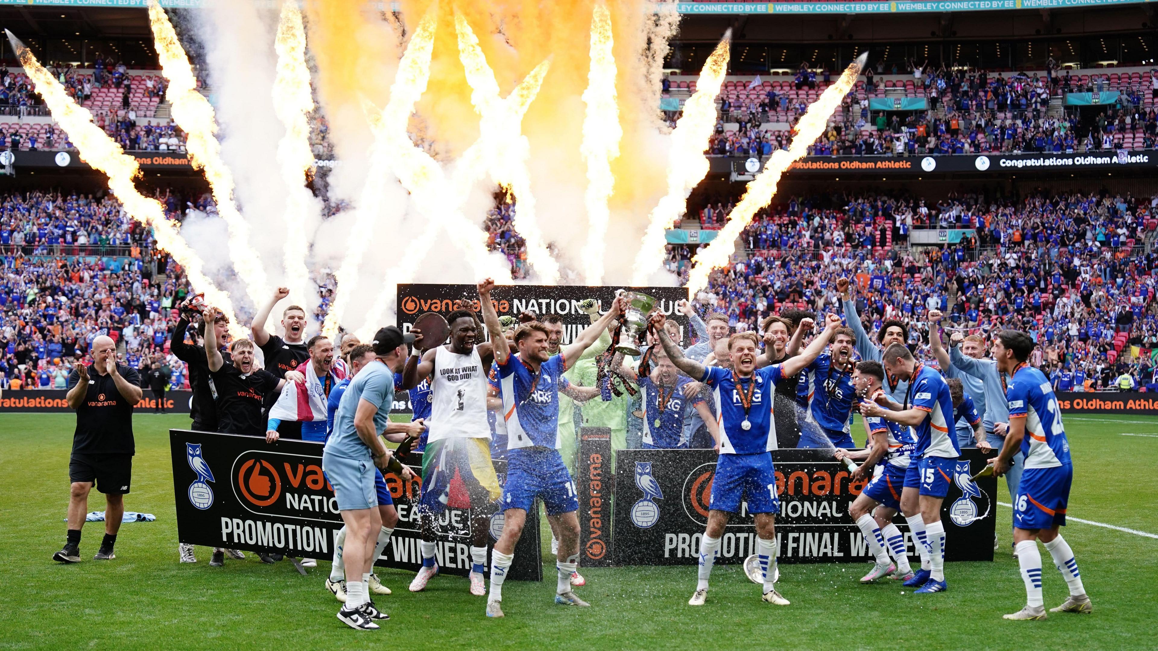 Oldham's players celebrating winning the National League promotion final at Wembley last season with pyrotechnics going off in the background
