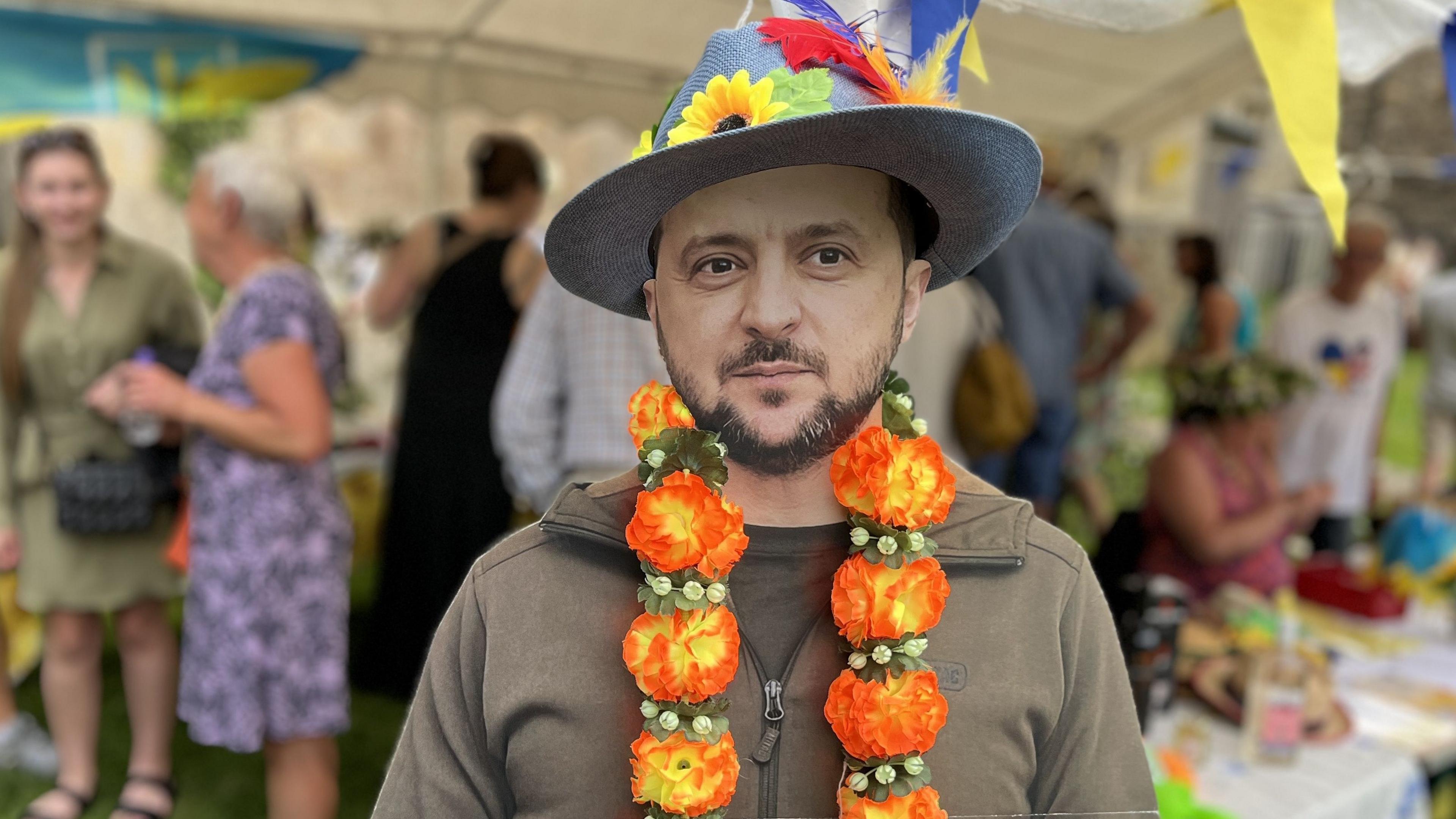 Cardboard cut-out of the Ukrainian President, Volodymyr Zelenskyy, in his military fatigues wearing a flower hat and flower garland.