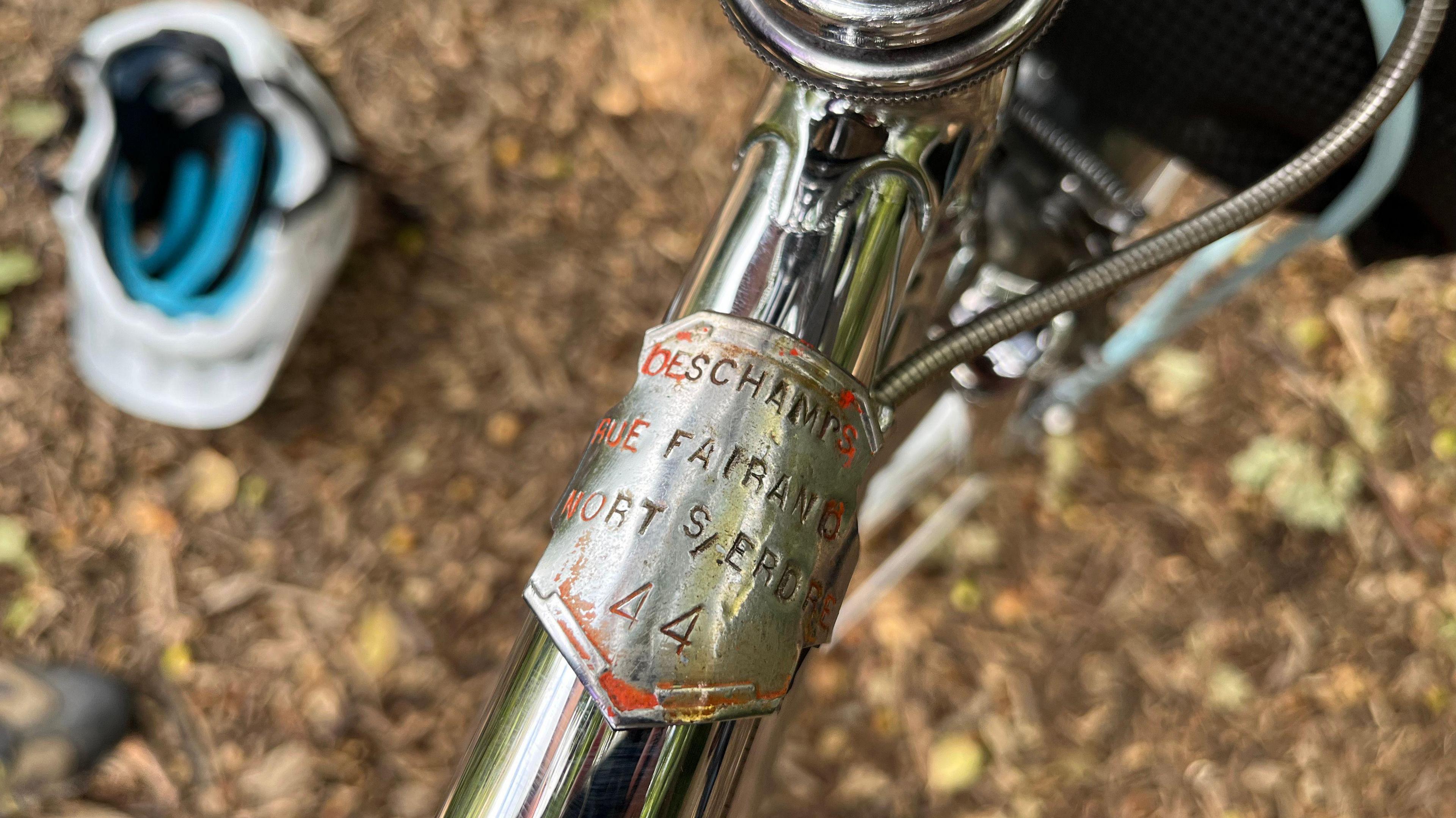 A metal licence plate which has an address on it and the name Deschamps and 1944 on it. It is on the frame of the bike