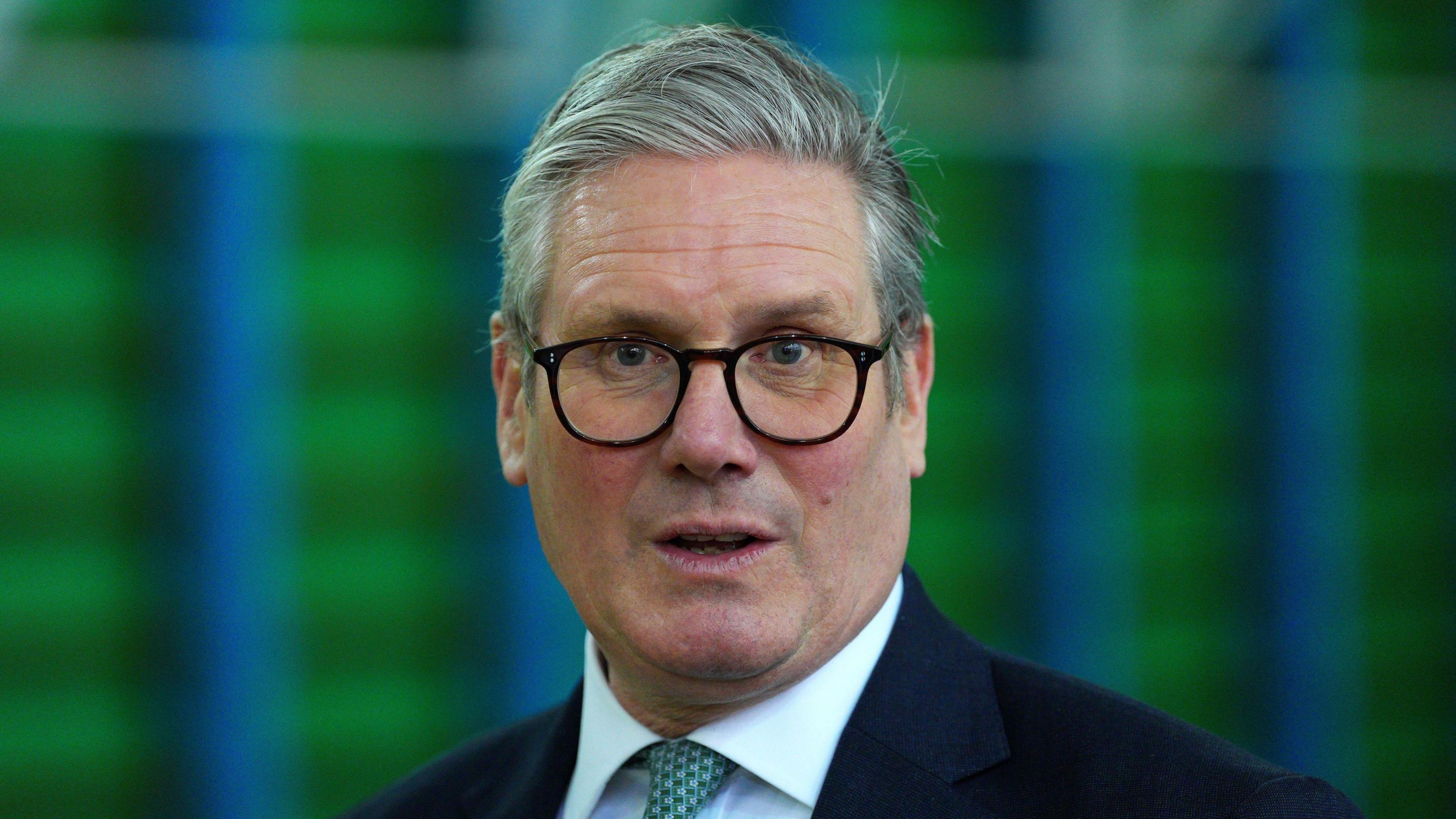 Keir Starmer, who has grey hair and is wearing dark glasses and a green tie and white shirt