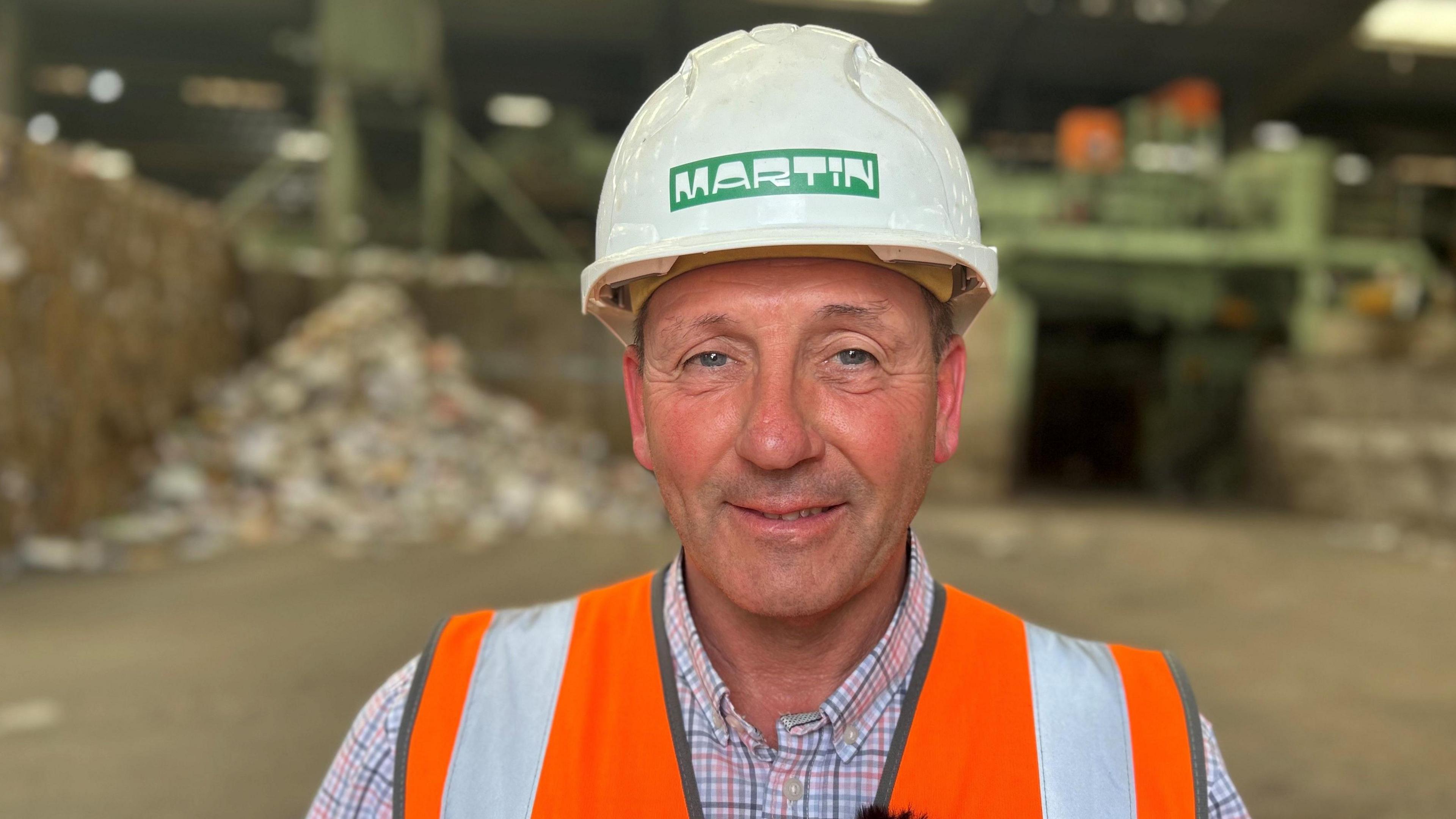 Declan Nortcliffe, Operations Director of H Martin in orange high vis vest and a white hard hat with piles of waste behind him