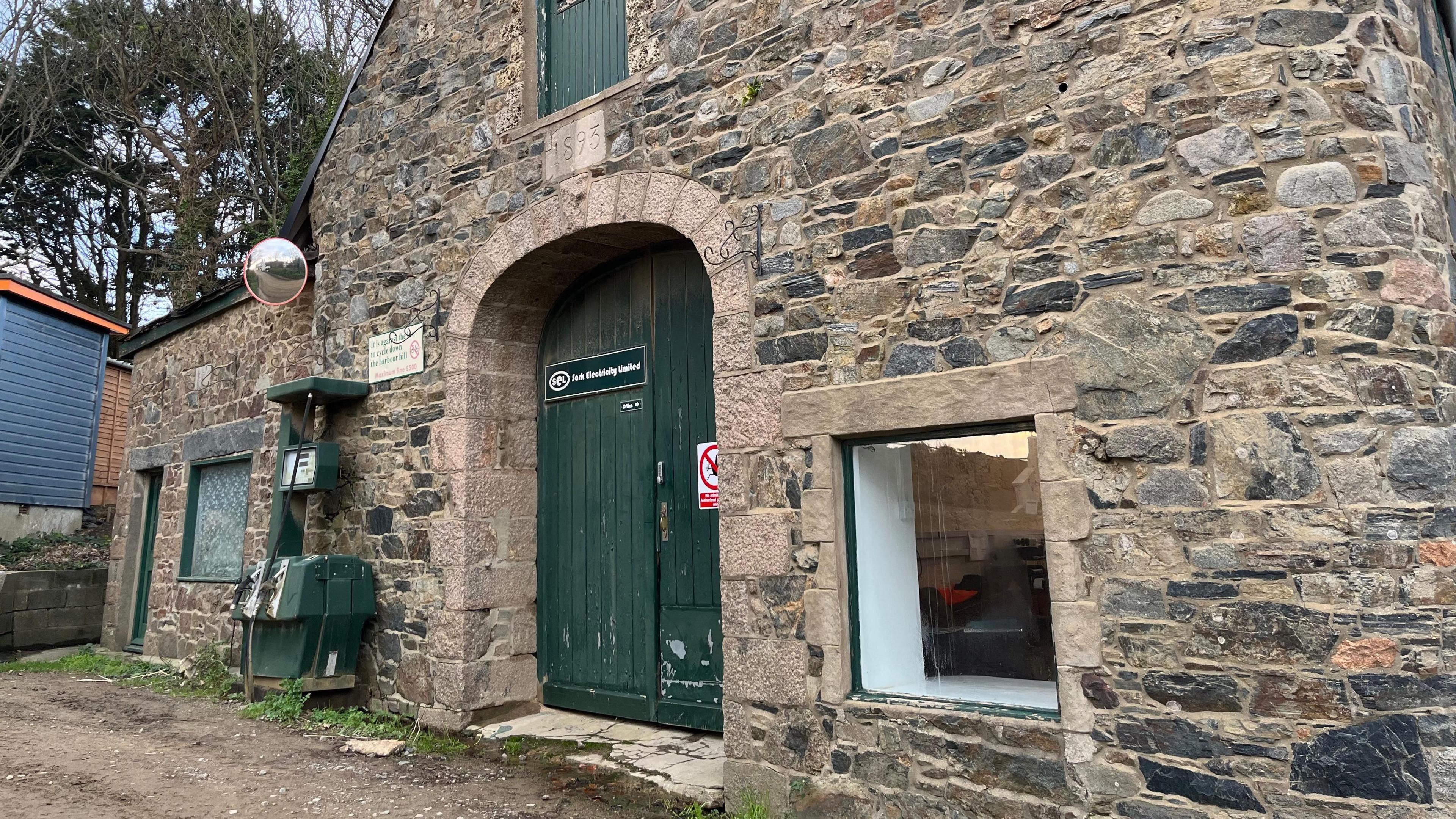 A brick building with a wooden green door and a sign which says Sark Electricity Limited. 