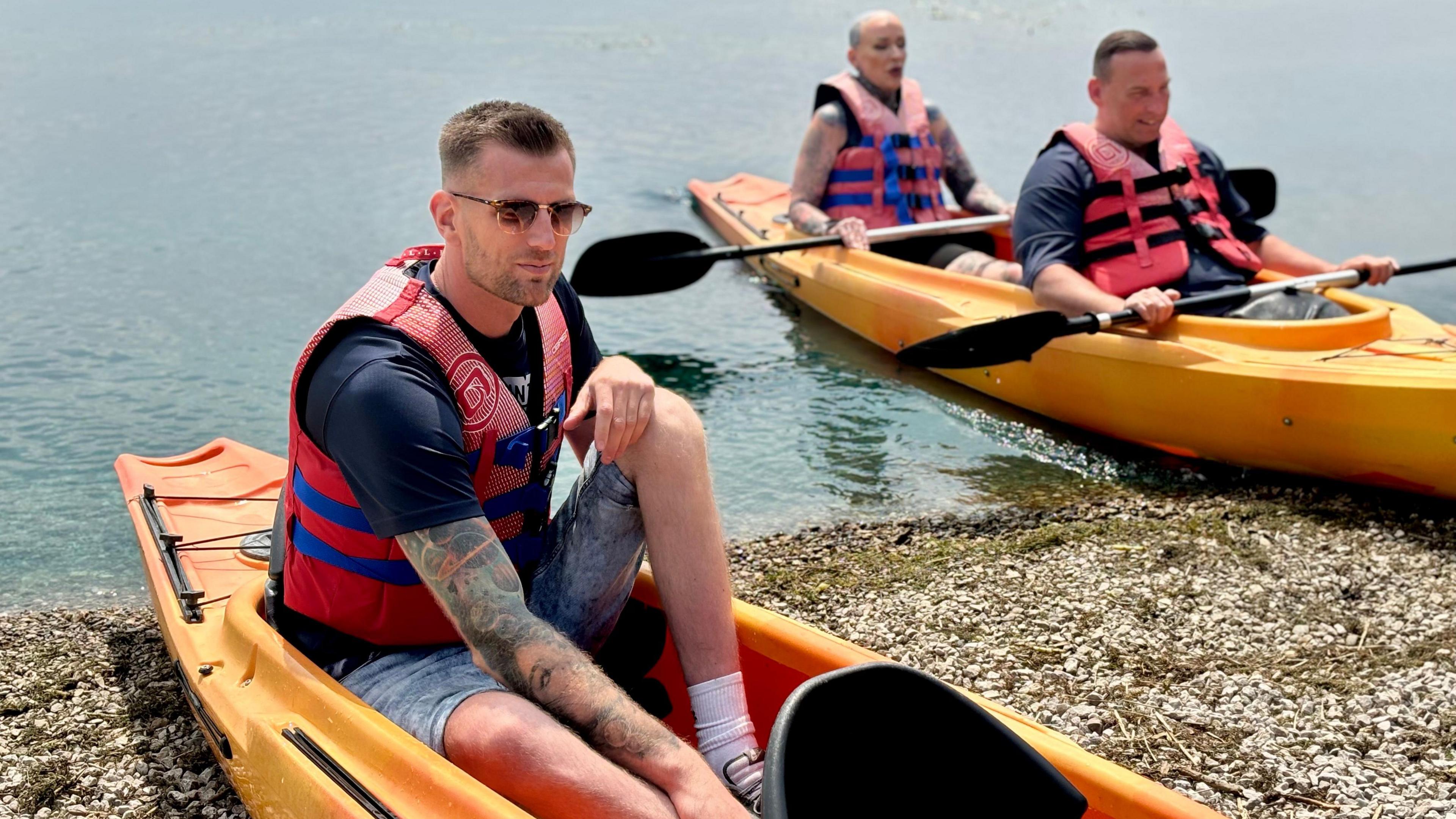 The three canoeists sitting in their boats at the shoreline during a training session