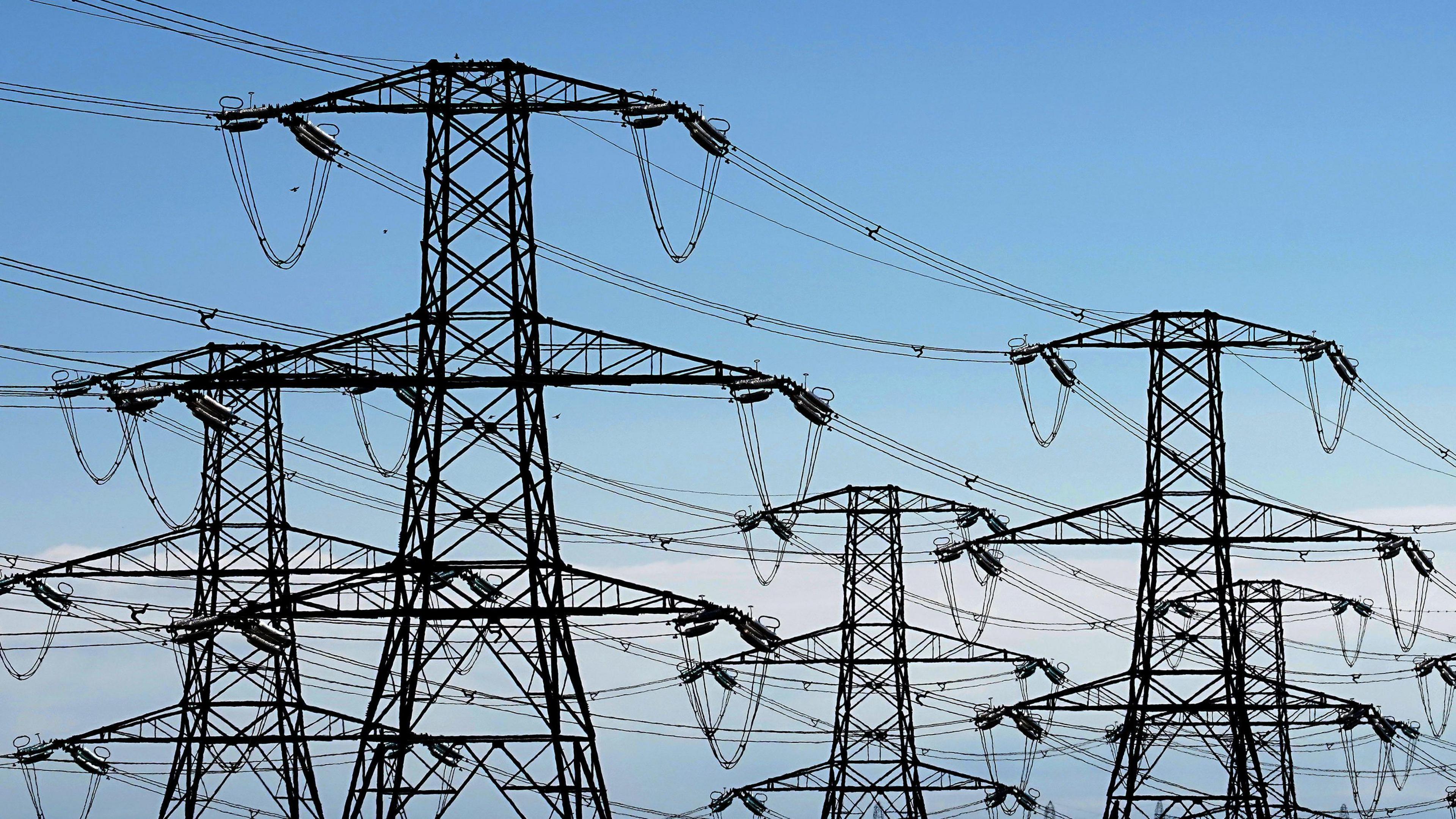 Four closely-packed pylons, linked by wires, against a pale blue sky