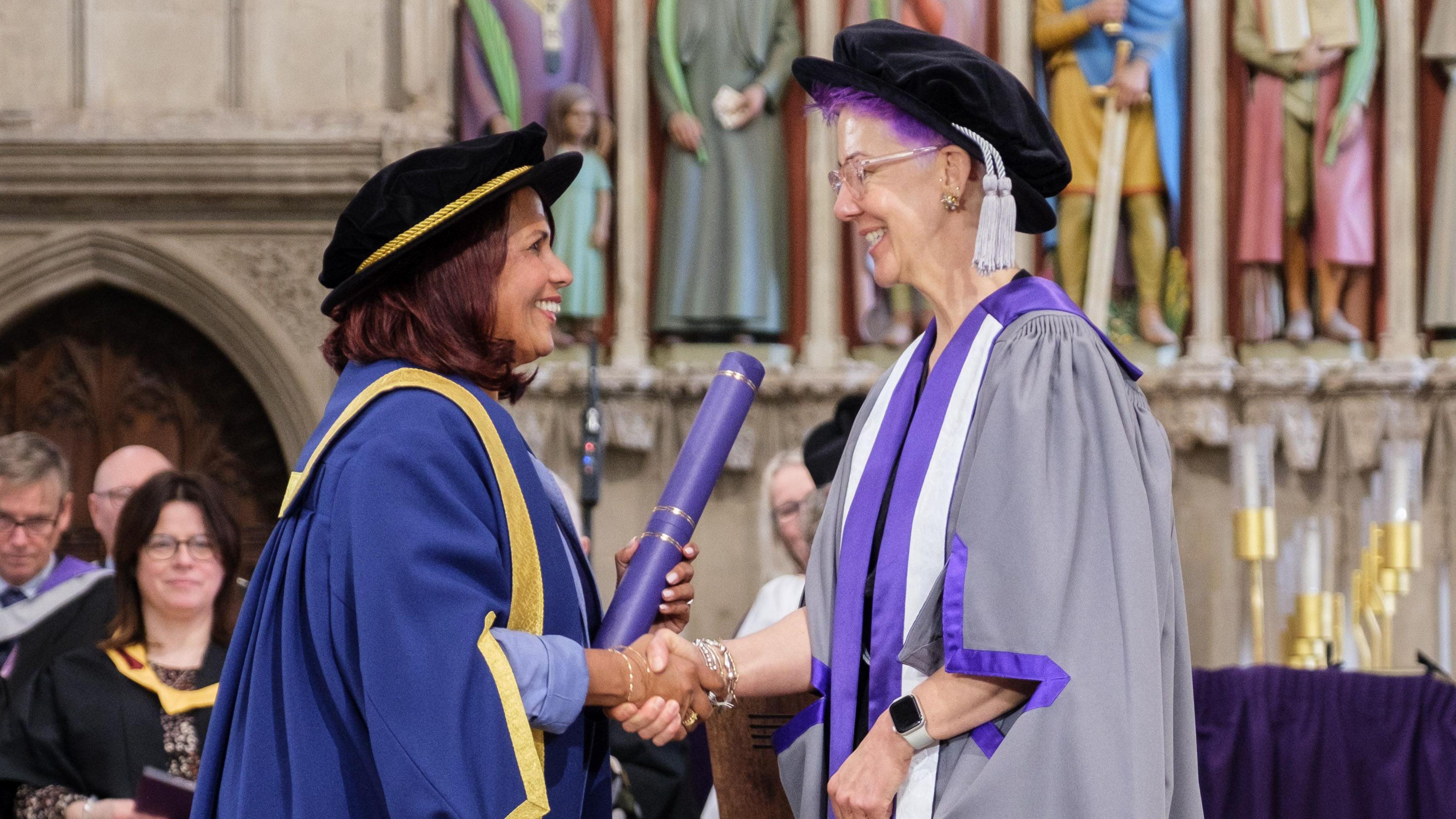 Rebecca Platt is shaking hands with a member of University staff as she accept her Fellowship