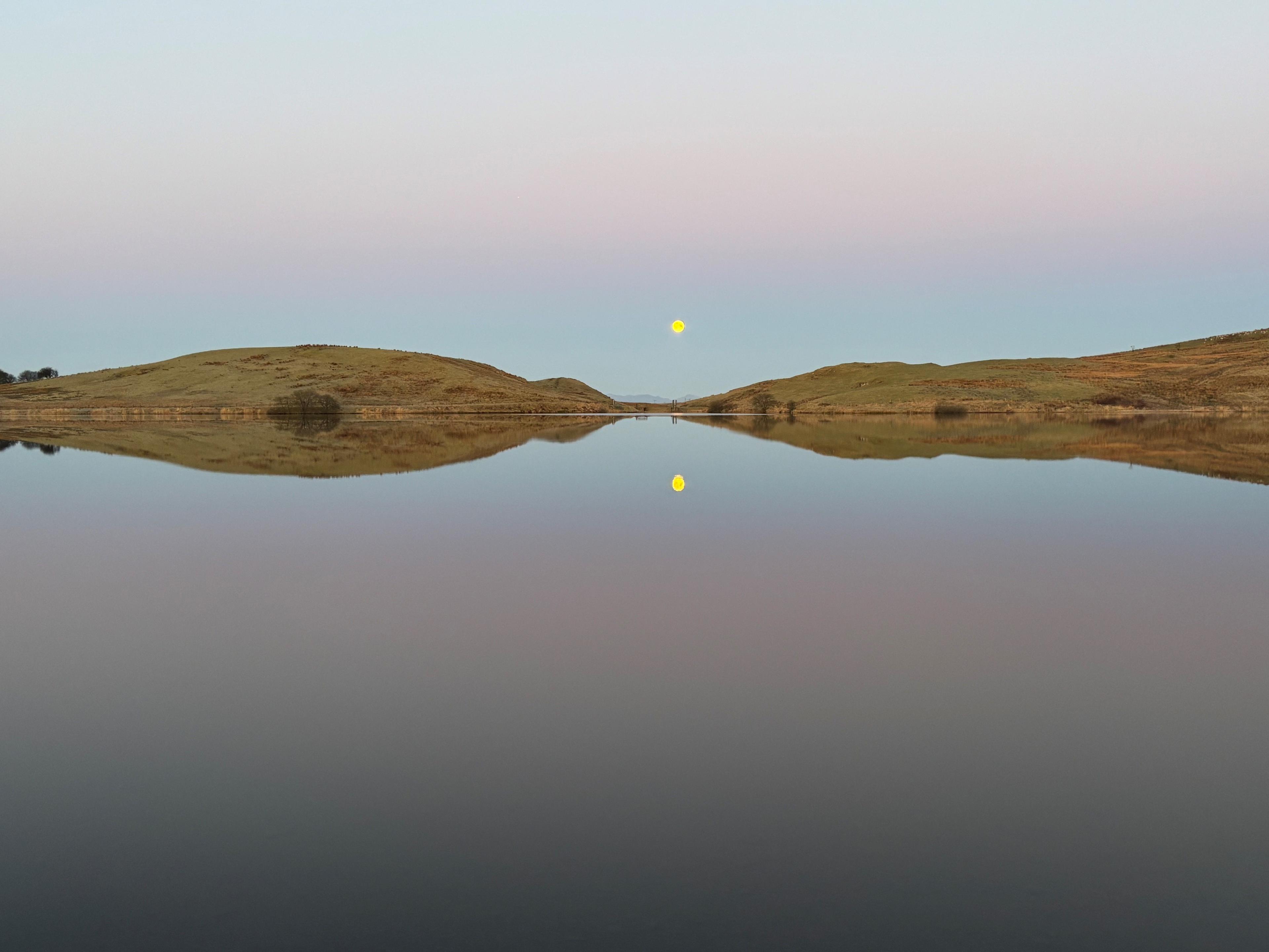 Two hills and the sun reflected on the surface of a loch.