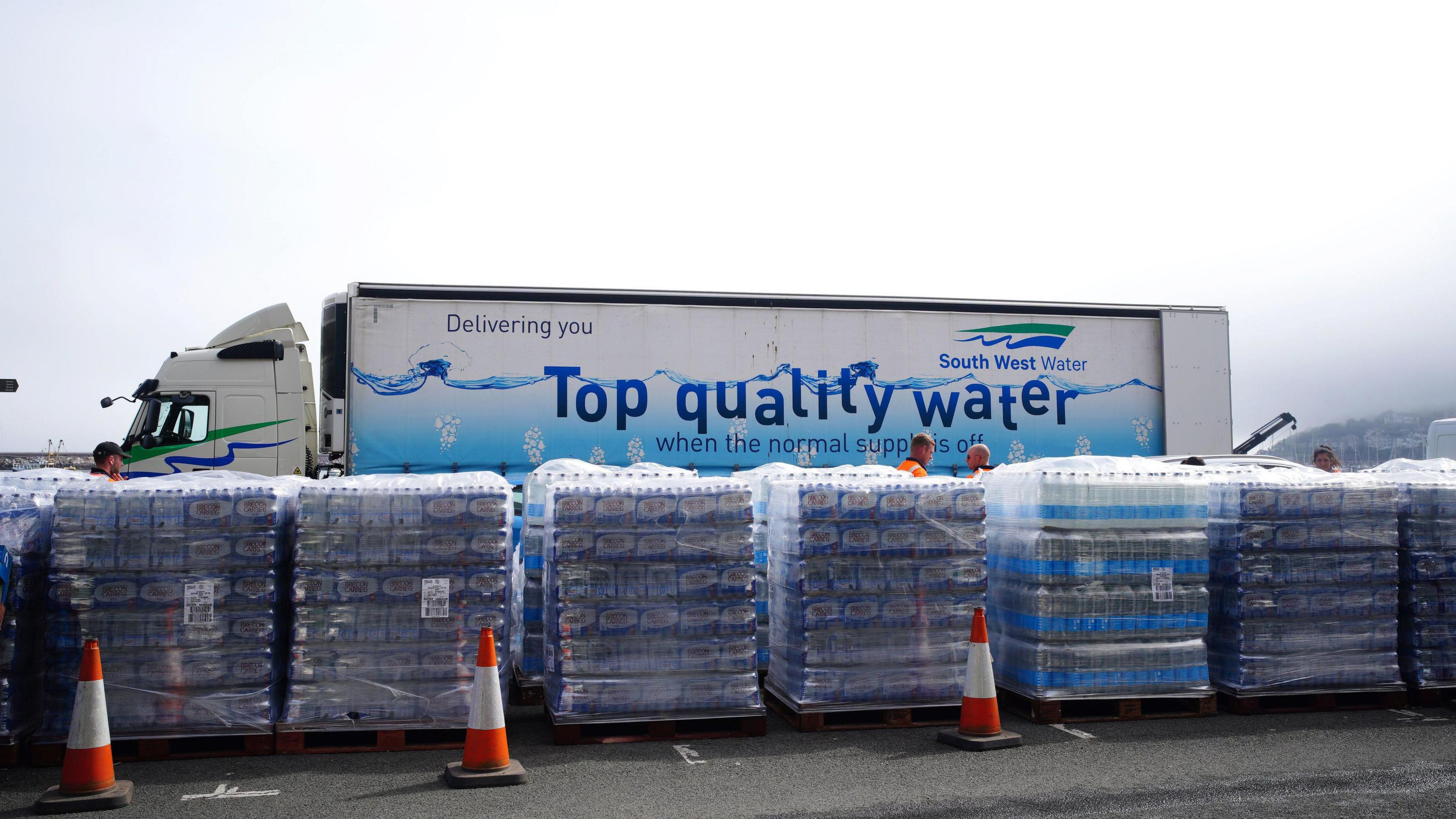 A lorry that says "top quality water" parked behind pallets of water