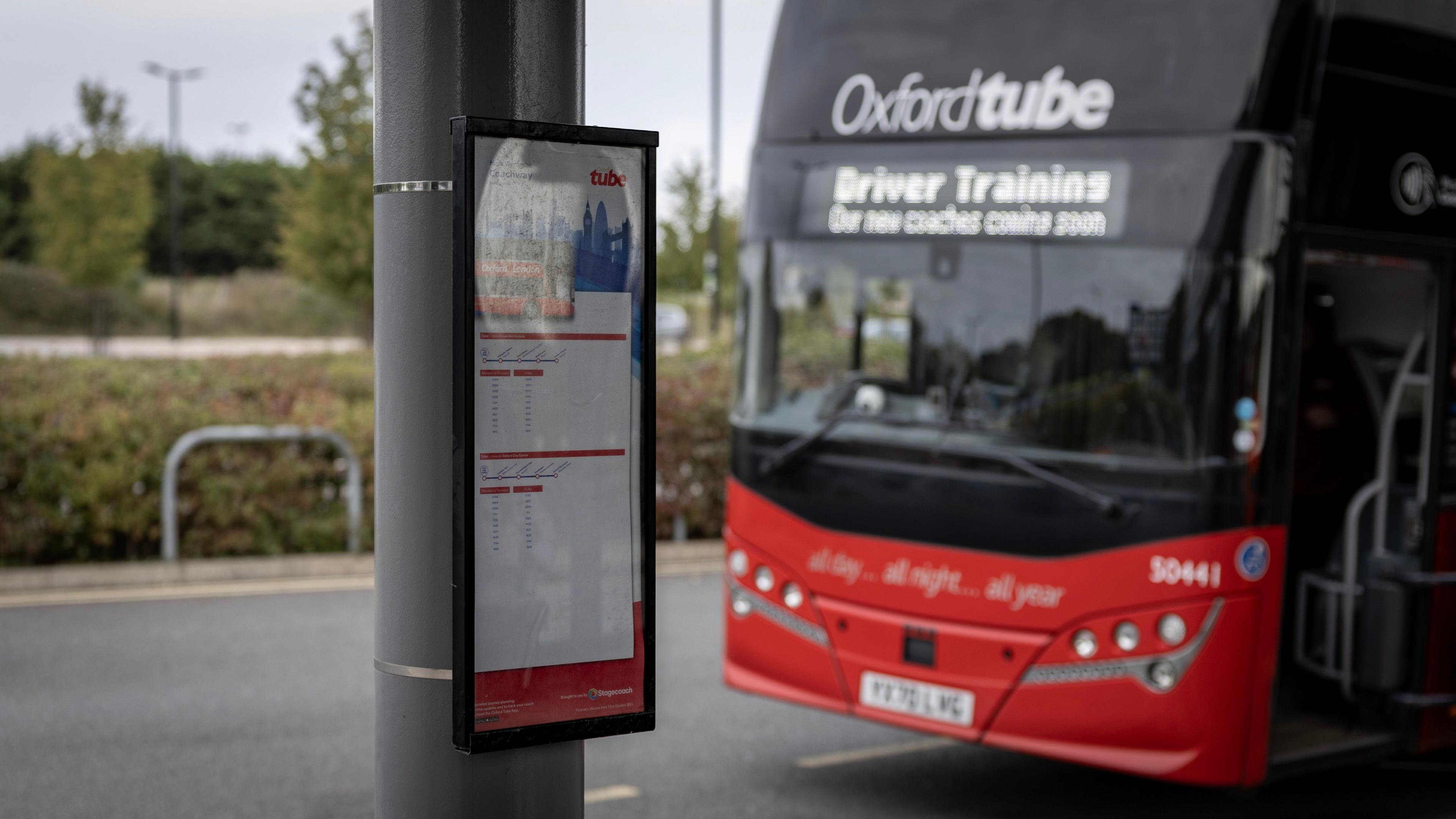a bus timetable on a pole with a bus in the background