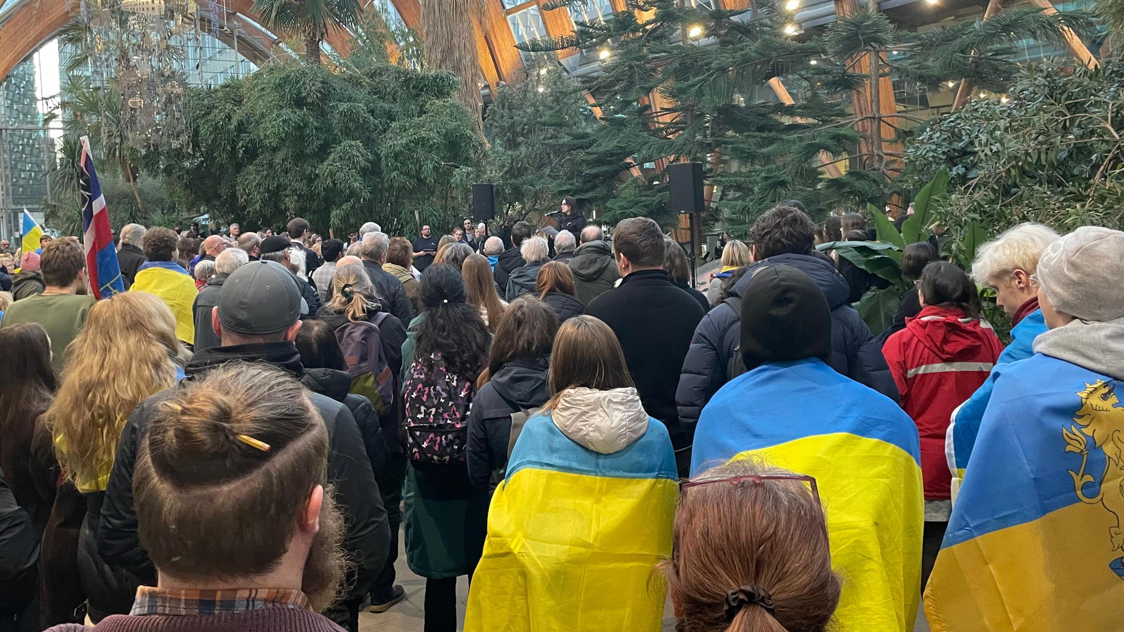 People are gathered inside the Winter Garden to listen to one of the guest speakers.