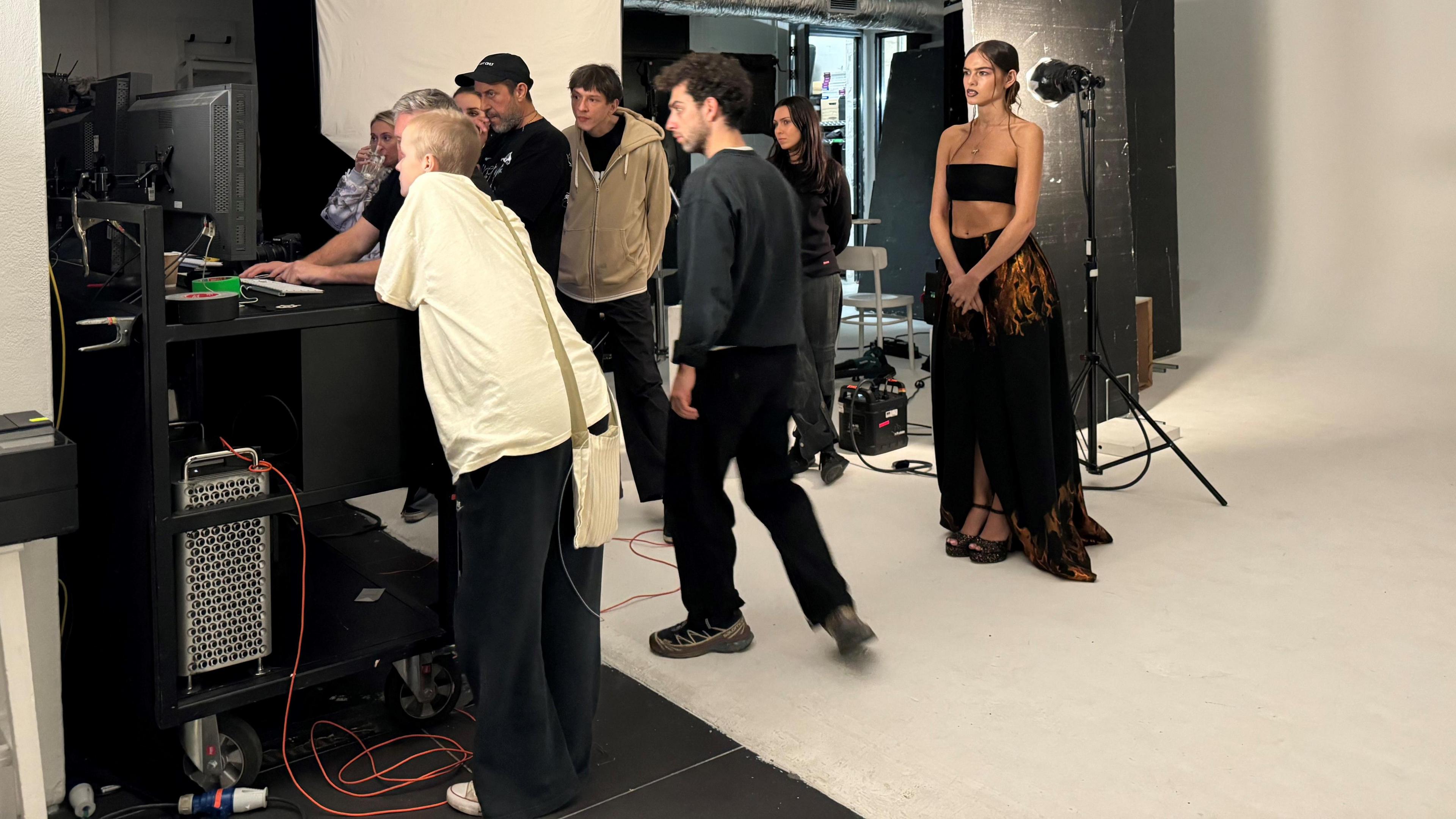 Liz looking at a computer screen with Ranking and five other people. There is a model in the background wearing a black long flowing skirt and a black bandeau top