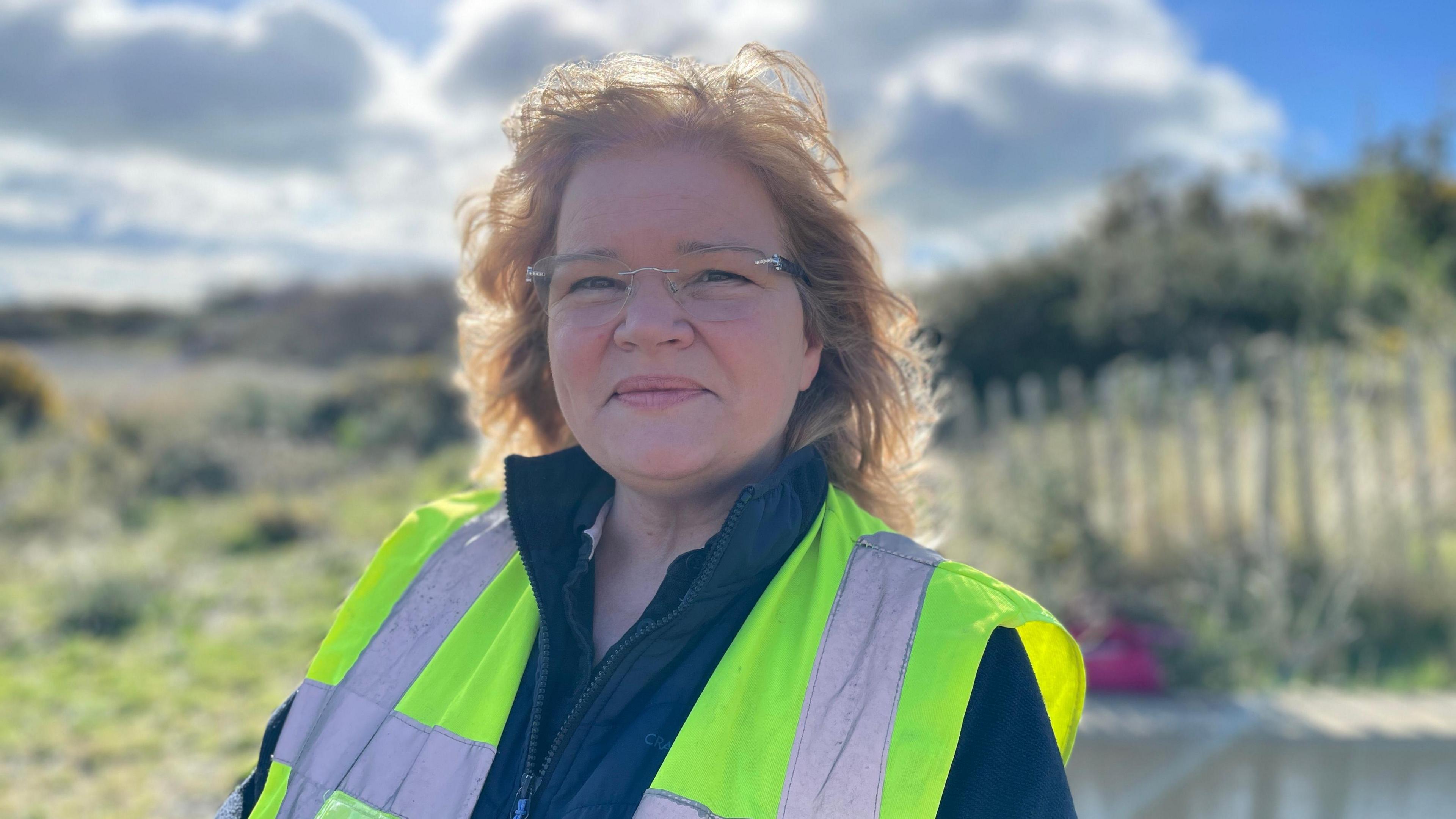 RNLI volunteer Caroline Jones, portrait stood on beach, wearing hi-vis vest